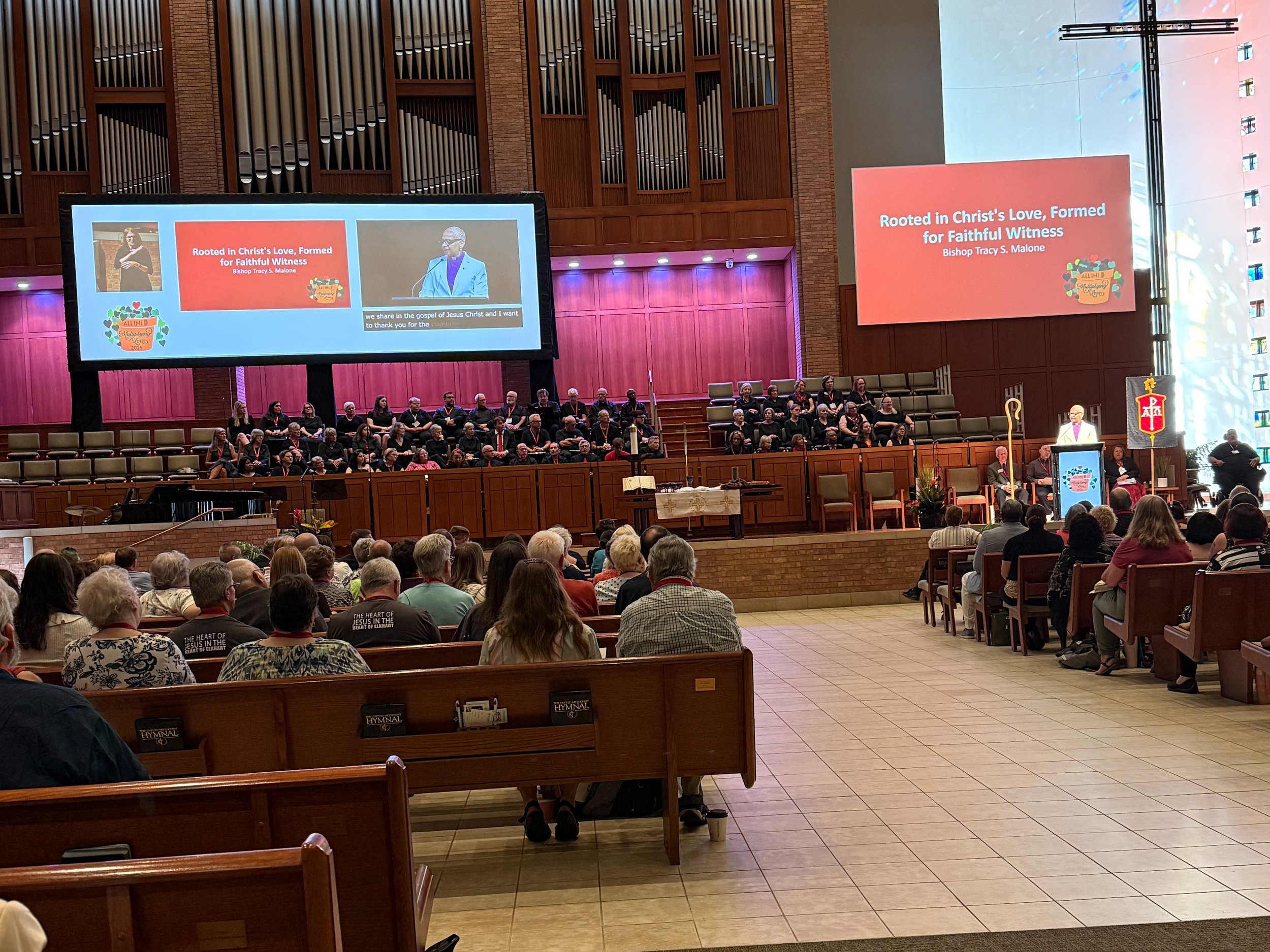 picture of a church sanctuary during Annual Conference showing a screen with captioning and ASL