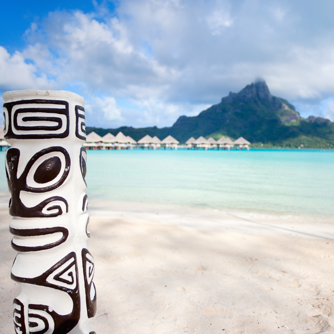 Carved Polynesian tiki art on a white-sand beach with overwater villas in Bora Bora