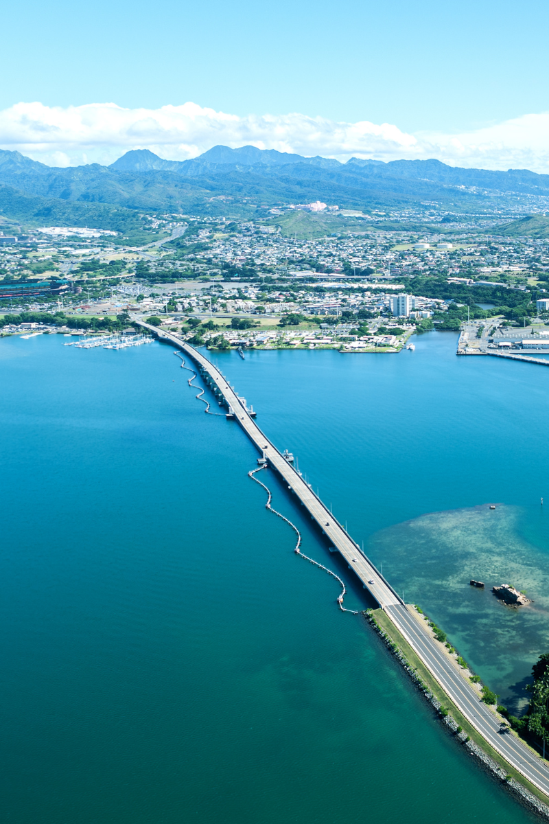 Aerial view of the Admiral Clarey Bridge spanning the bright blue waters of Pearl Harbor toward Ford Island on Oahu.