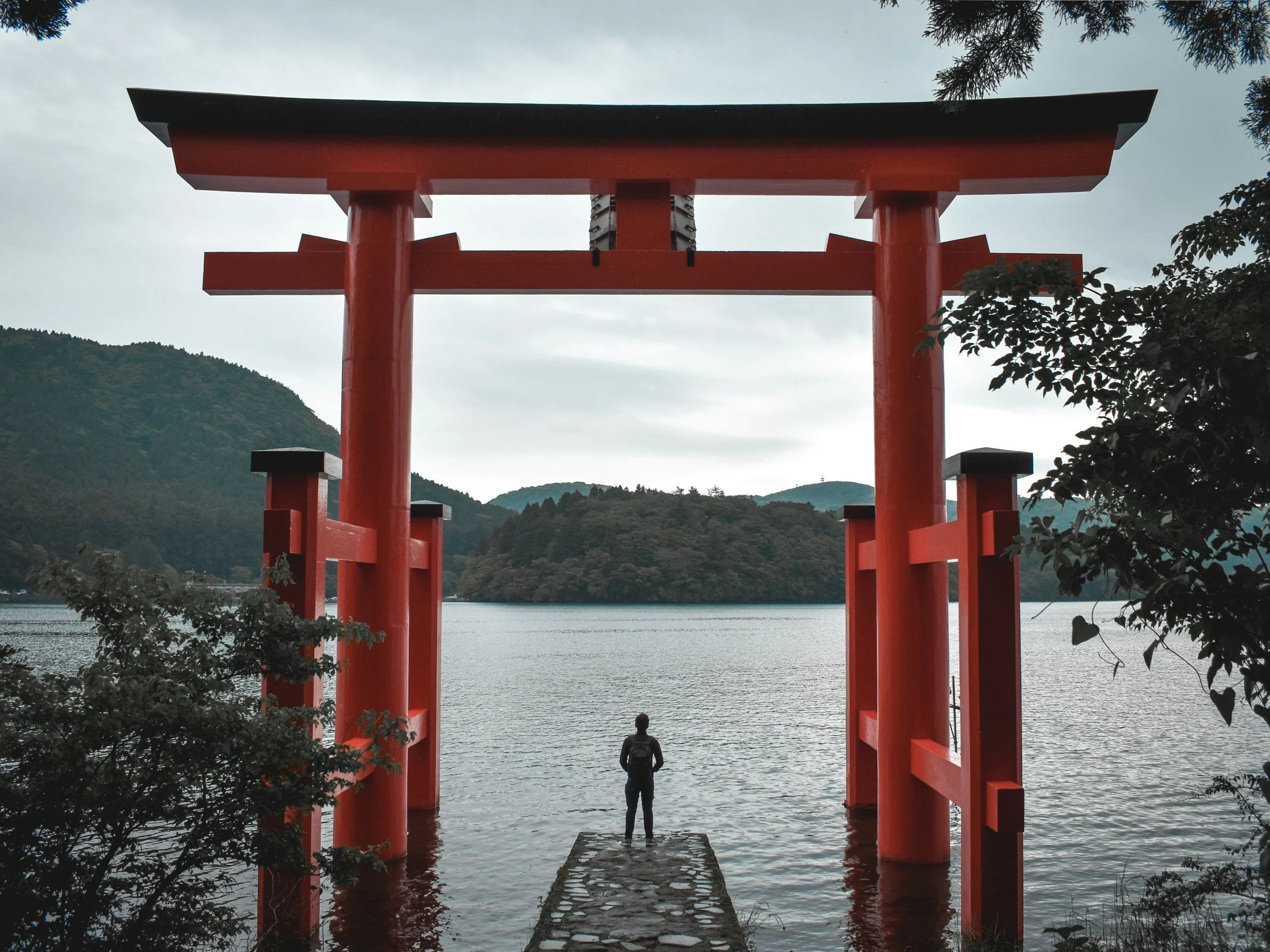 A traveler standing before a massive red Torii gate overlooking a serene lake in Japan.