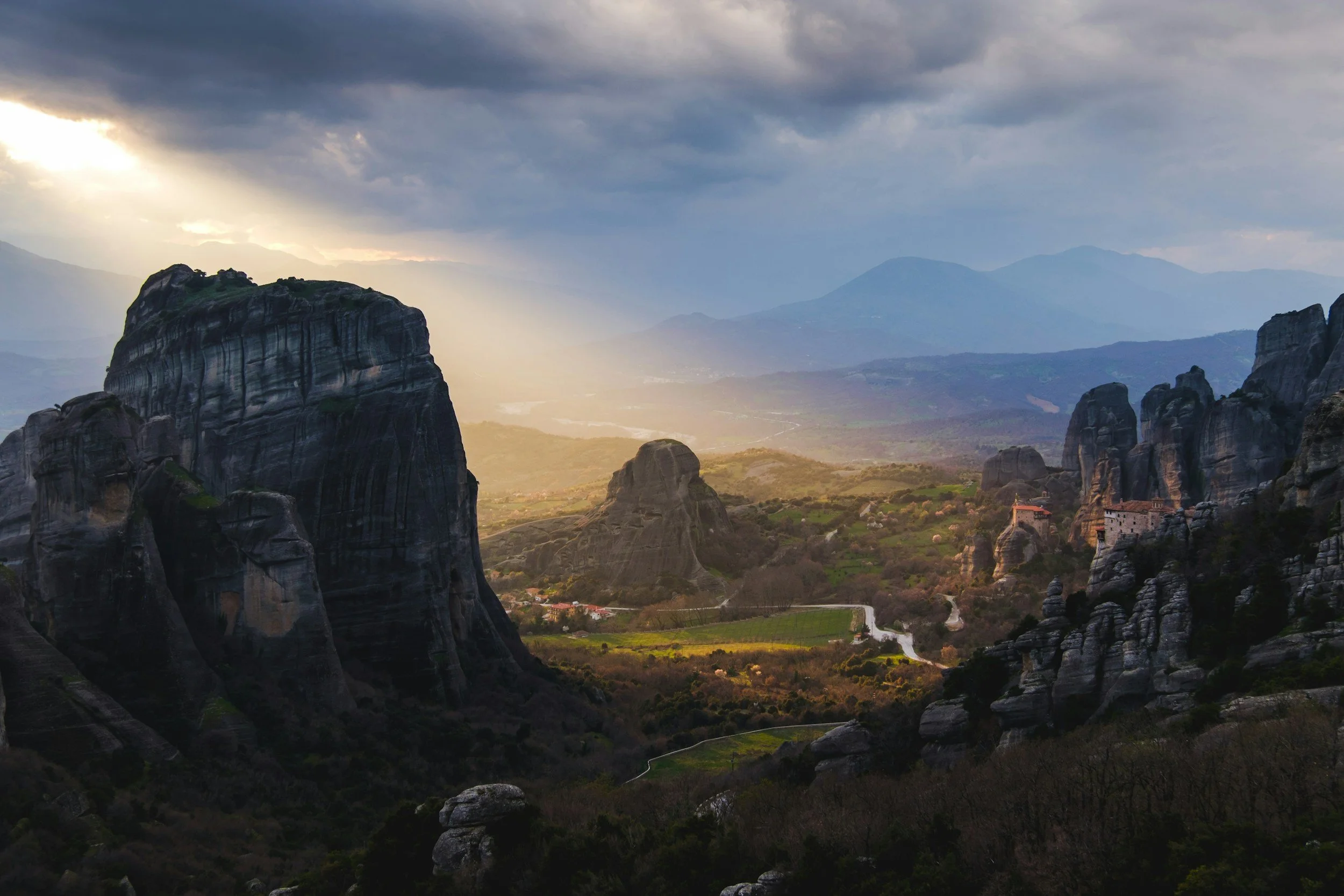 Dramatic rock formations and ancient monasteries of Meteora, Greece, at sunset with golden light hitting the valley, curated by Lavishly Travel