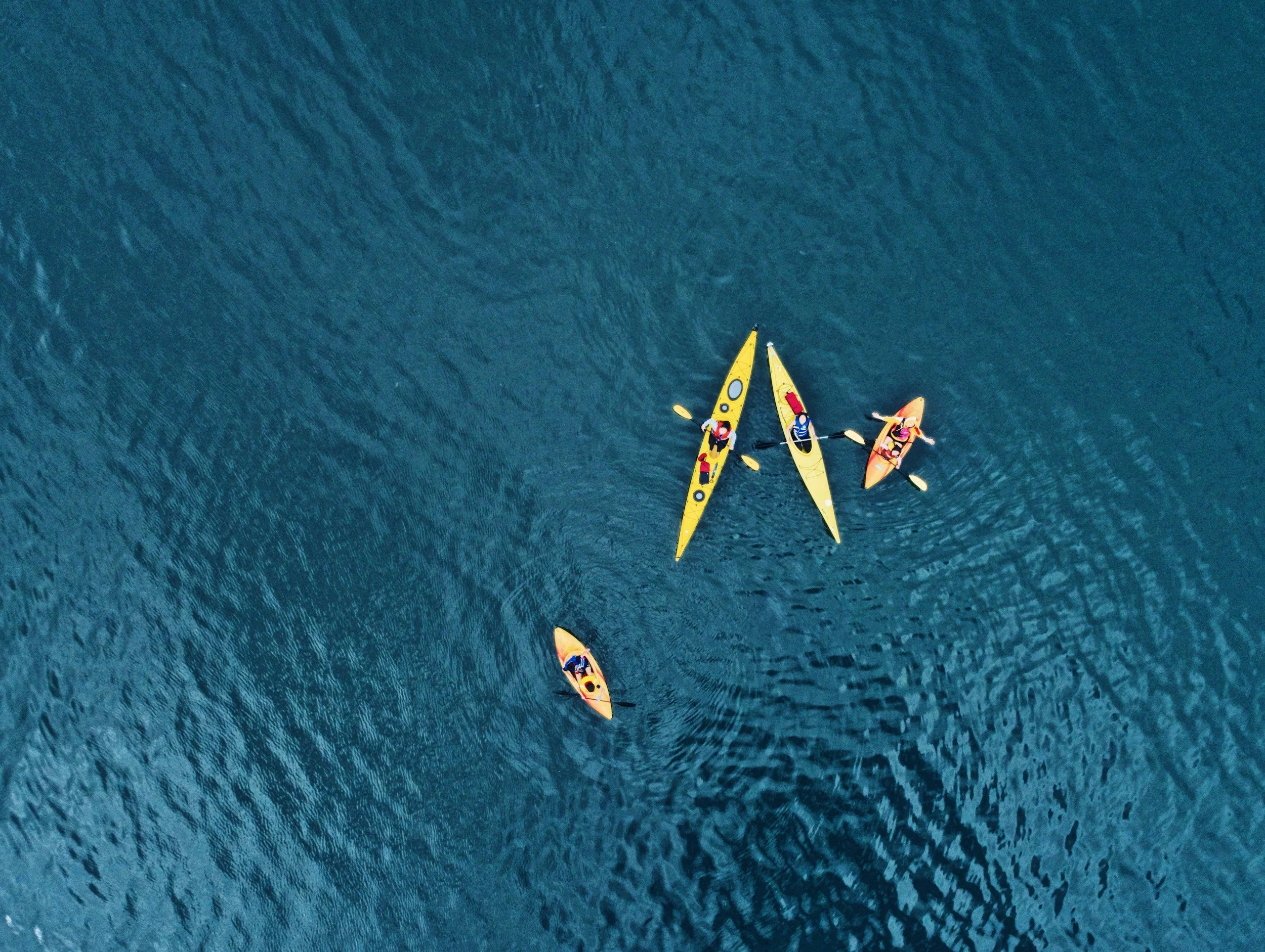 Aerial view of four yellow kayaks paddling in deep blue Caribbean waters. An engaging group activity for multi-generational family vacations and tropical water sports adventures.
