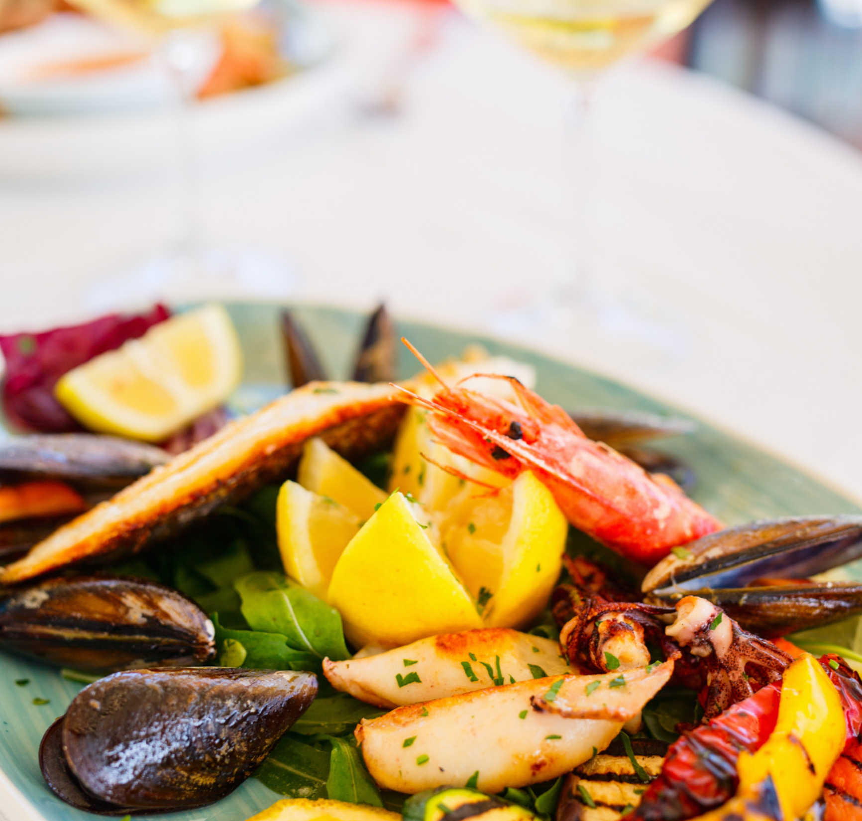A plate of mixed seafood with mussels, prawns and lemon wedges on a restaurant table.