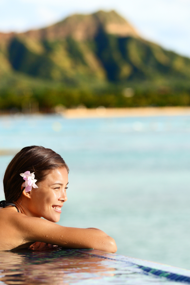 Woman with a flower in her hair resting at the edge of a pool overlooking a tropical bay