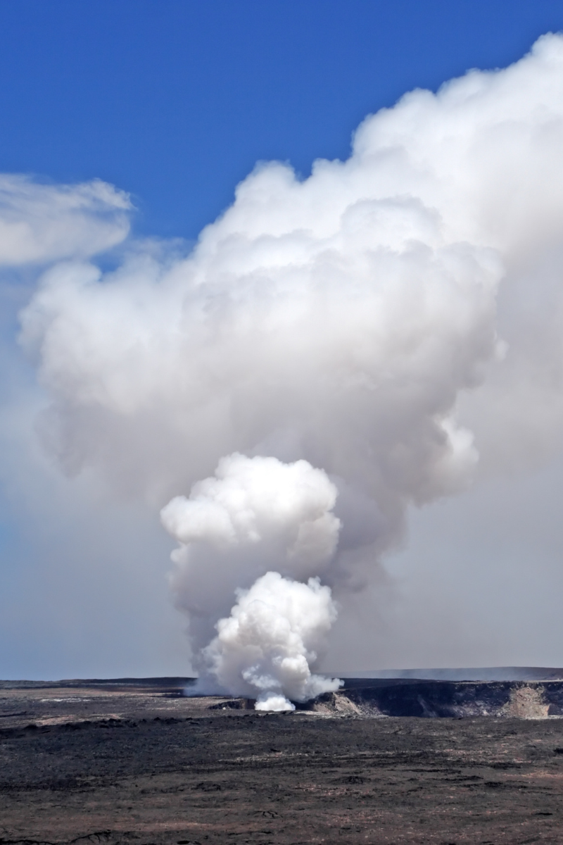 White volcanic plume rising above a dark crater landscape on Hawaii Island