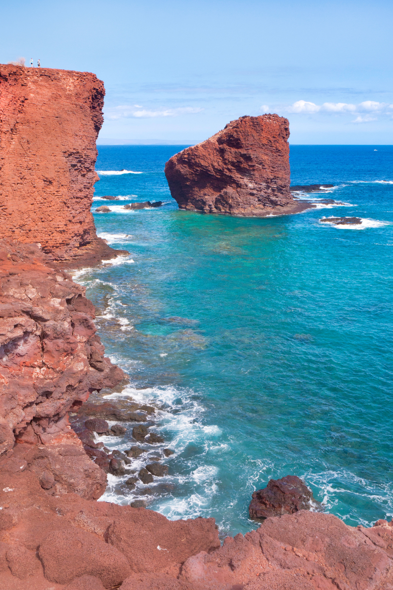 Red sea cliffs and an offshore rock rising above blue water on Lanai