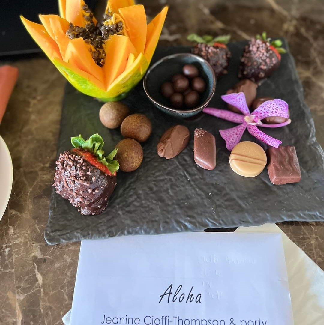 Experience authentic Hawaiian hospitality with luxury resort welcome amenities featuring fresh tropical fruit, artisan chocolates, and an orchid greeting.