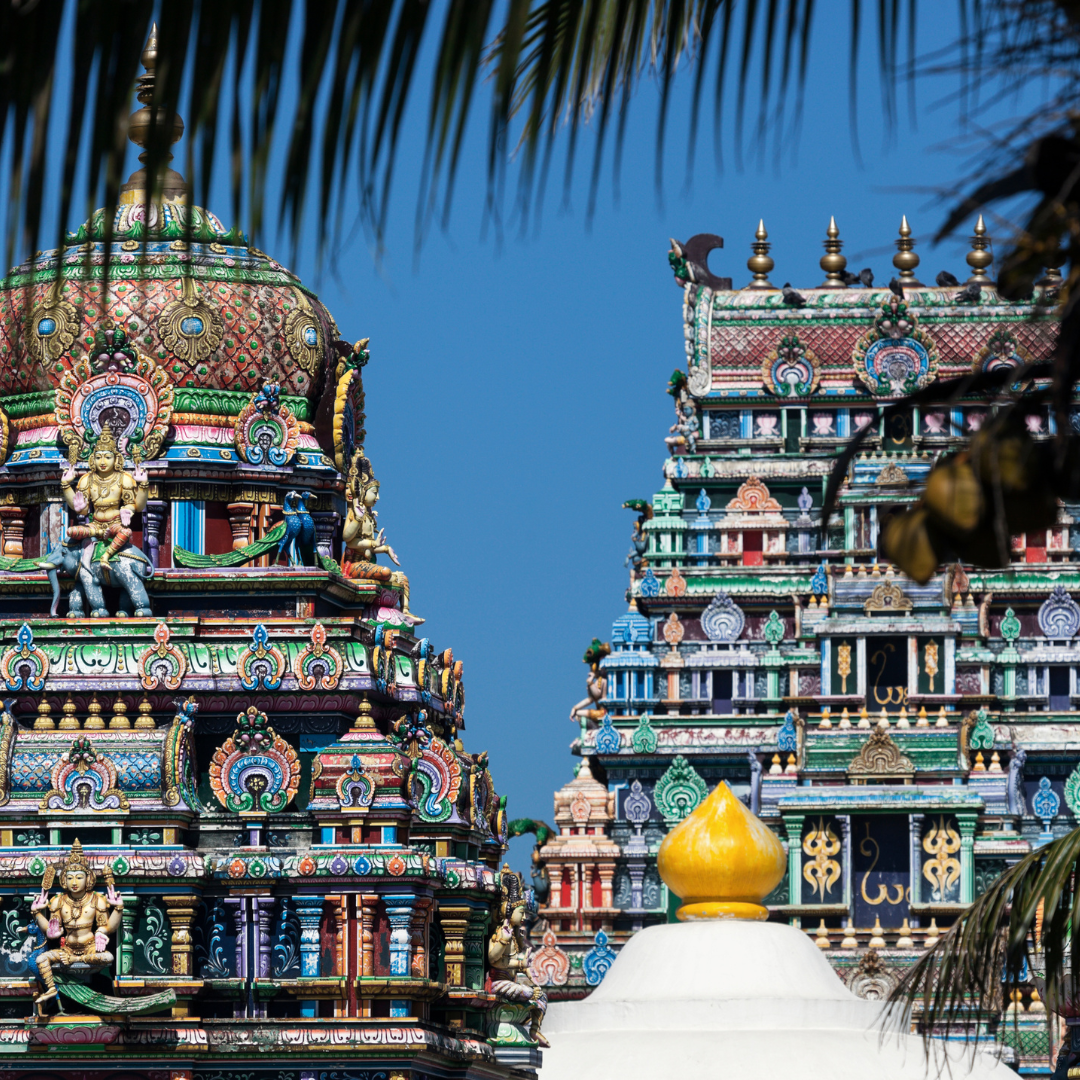 Close-up of the colorful, ornately carved towers of a traditional Dravidian-style Hindu temple against a blue sky.