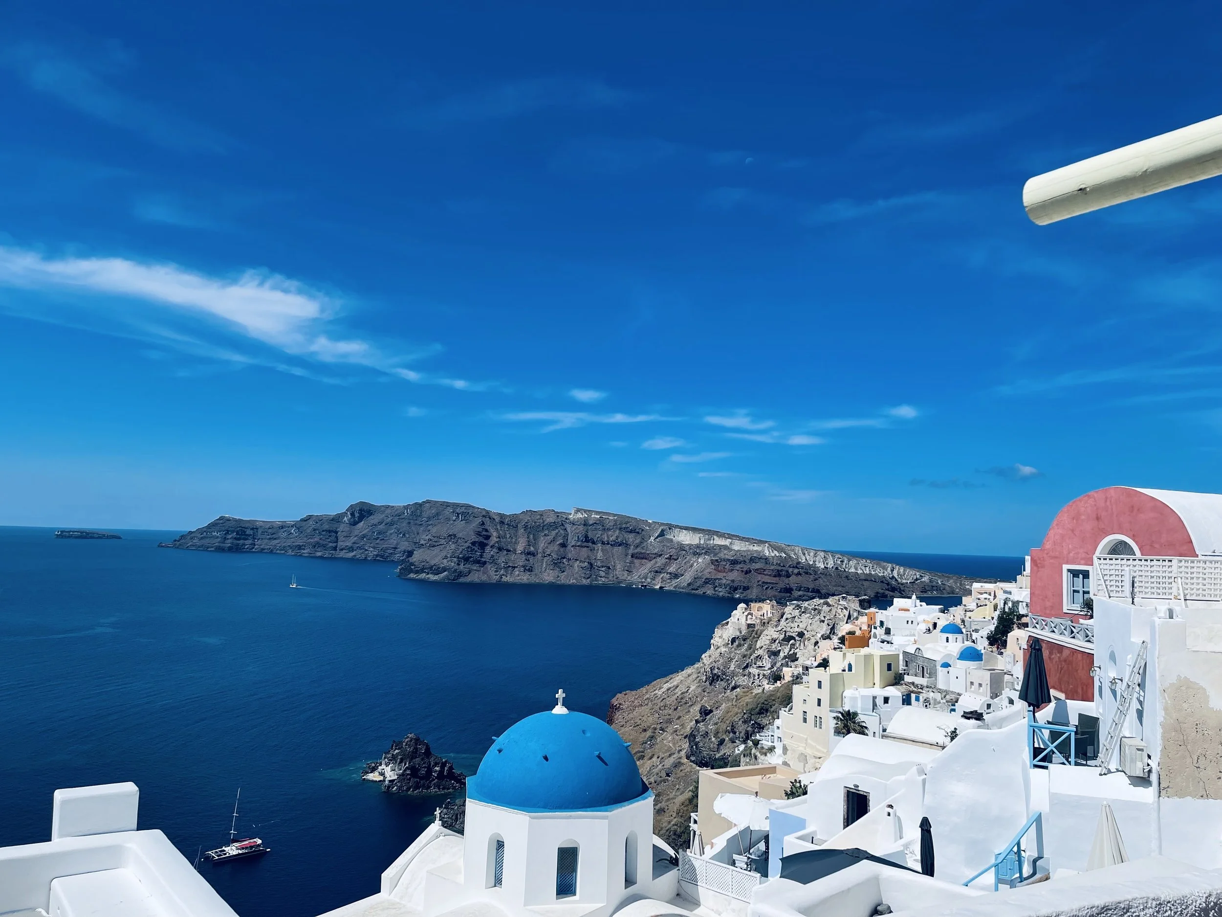Blue-domed church and whitewashed buildings above Santorini’s caldera and sea, photographed by Jeanine Cioffi.