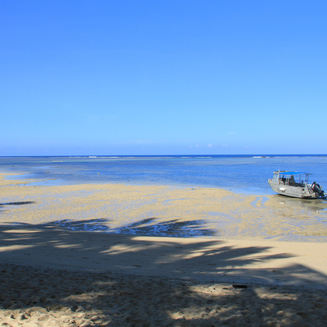 A small motorboat resting on a sunny, shallow sandbar at a tropical beach under a clear blue sky.