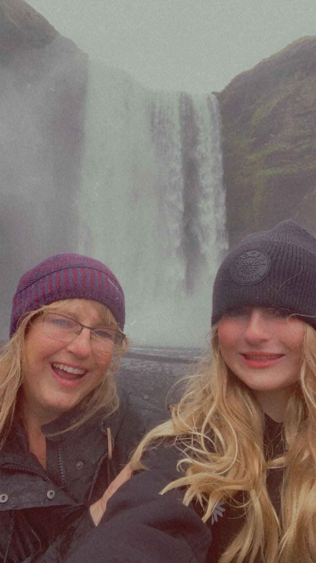 Jeanine Cioffi and her daughter in winter hats in front of a waterfall during their 2023 Iceland stopover