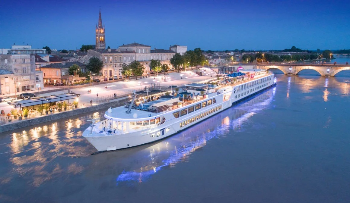 A luxury European river cruise ship docked along a historic city waterfront at twilight. An ideal travel option for exploring multiple European destinations in comfort and style.