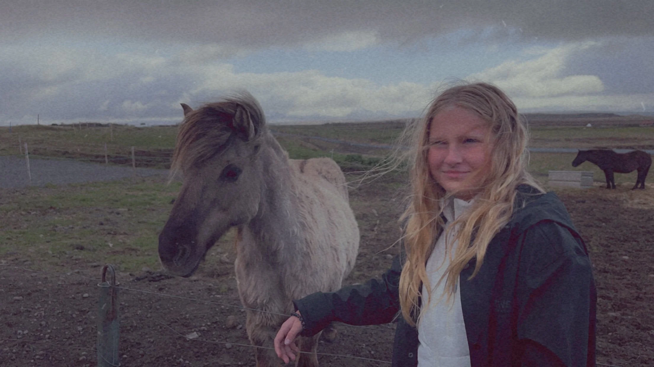 Jeanine's daughter smiling beside a shaggy Icelandic horse in a windswept pasture, photographed by Jeanine in Iceland