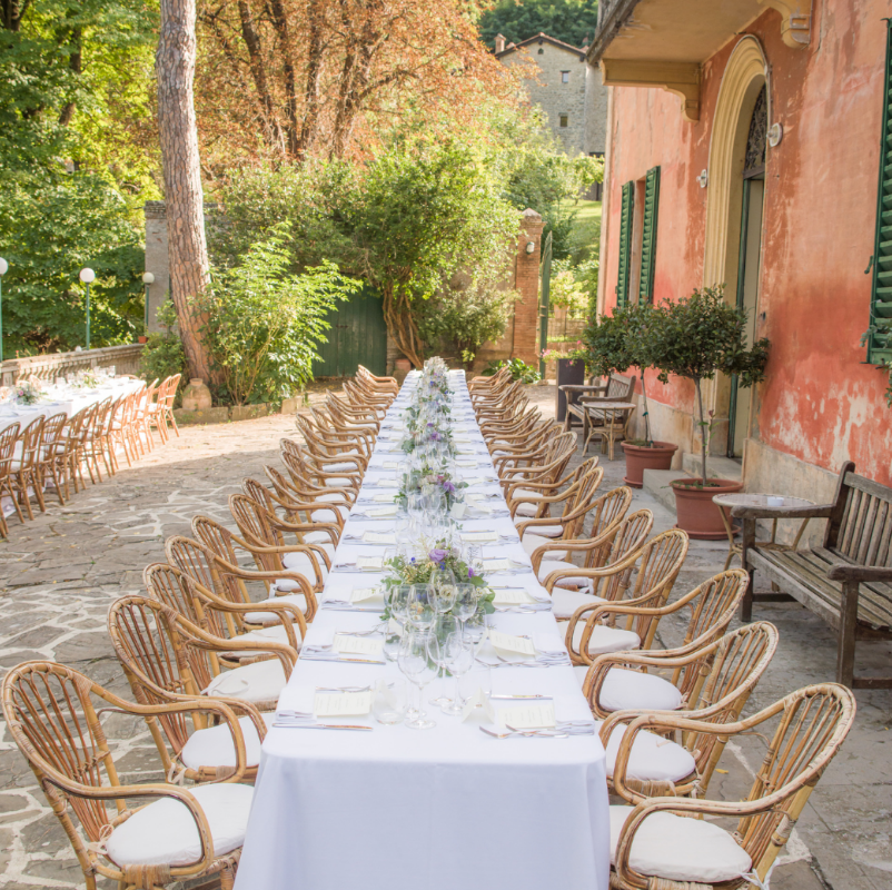 long, elegantly set outdoor wedding reception table at a rustic Italian villa with peach-colored walls.