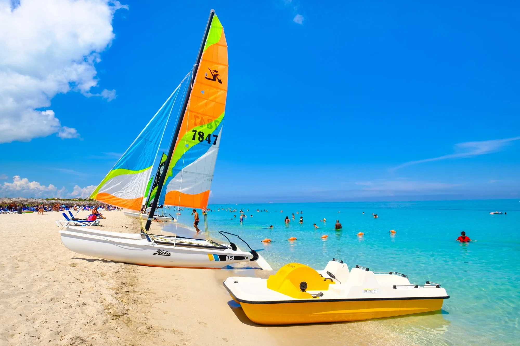 White sandy beach in Mexico featuring a small colorful sailboat and a yellow pedal boat on the shore. Ideal for family-friendly beach activities and coastal resort vacations.
