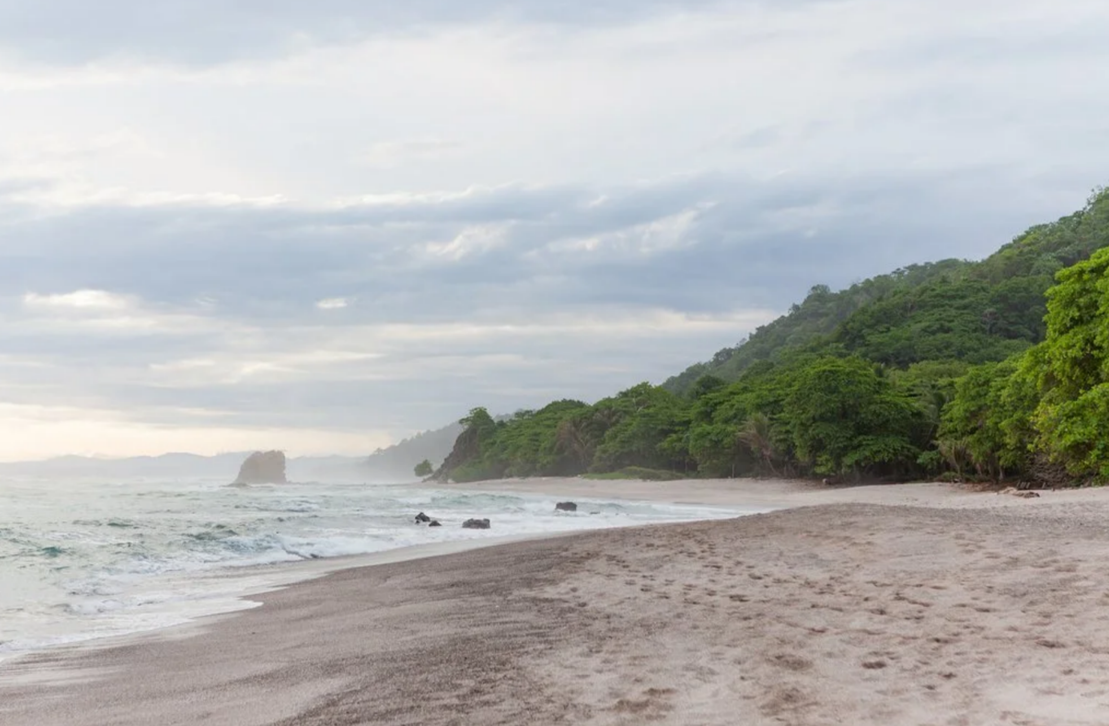 Escape to a secluded tropical beach in Costa Rica, where dense green jungle meets the soft sand and crashing waves of the Pacific Ocean.