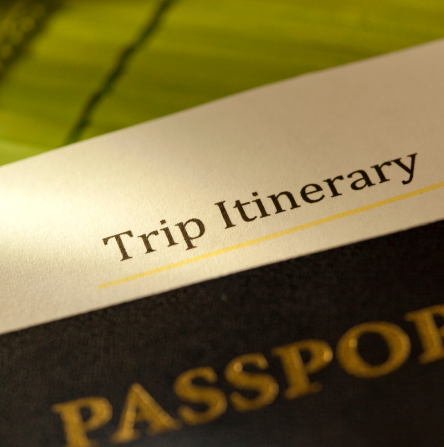 Extreme close-up of a printed paper reading Trip Itinerary resting on top of a dark passport cover.