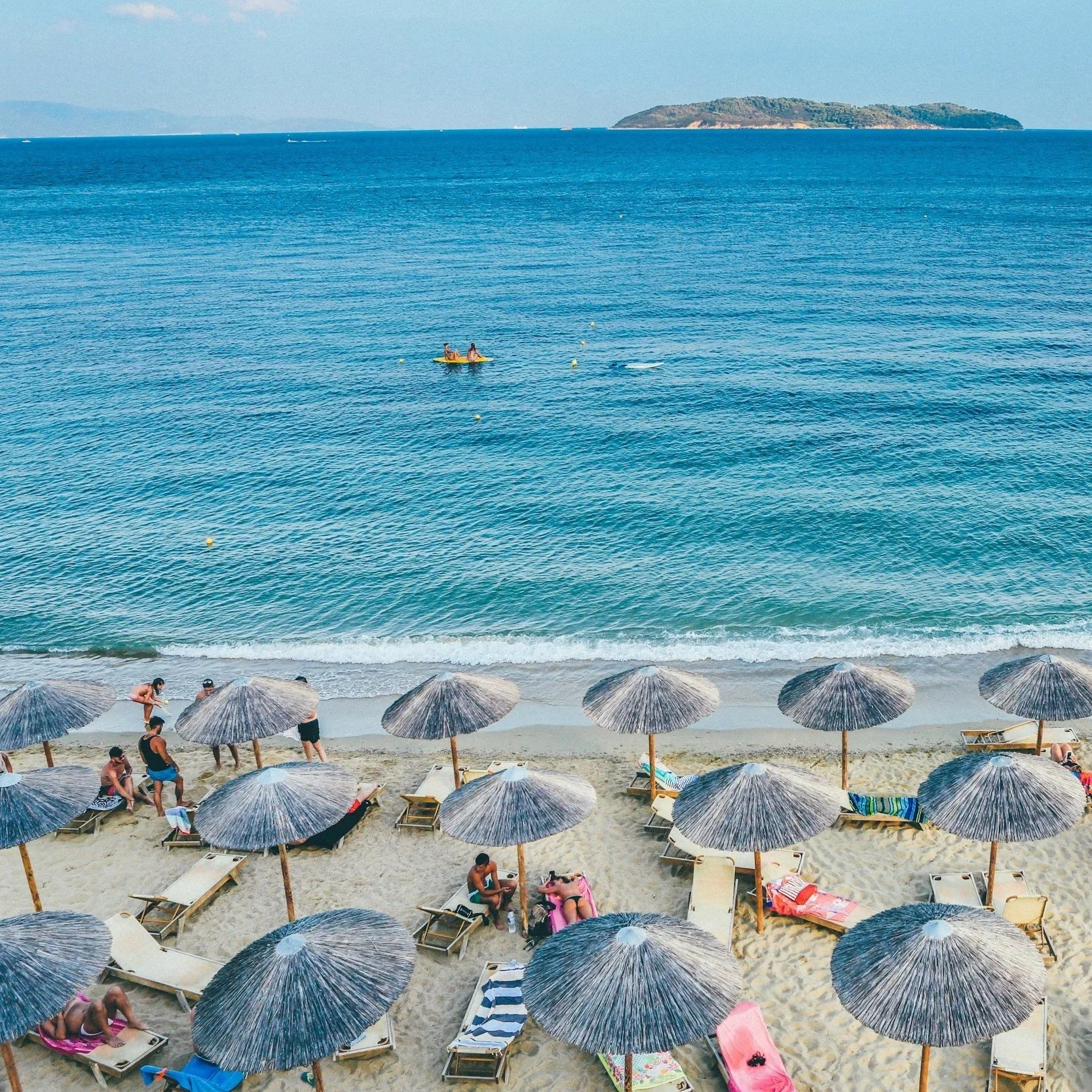 A luxury Greek beach with rows of thatched umbrellas and turquoise water, representing premium Mediterranean seaside vacations