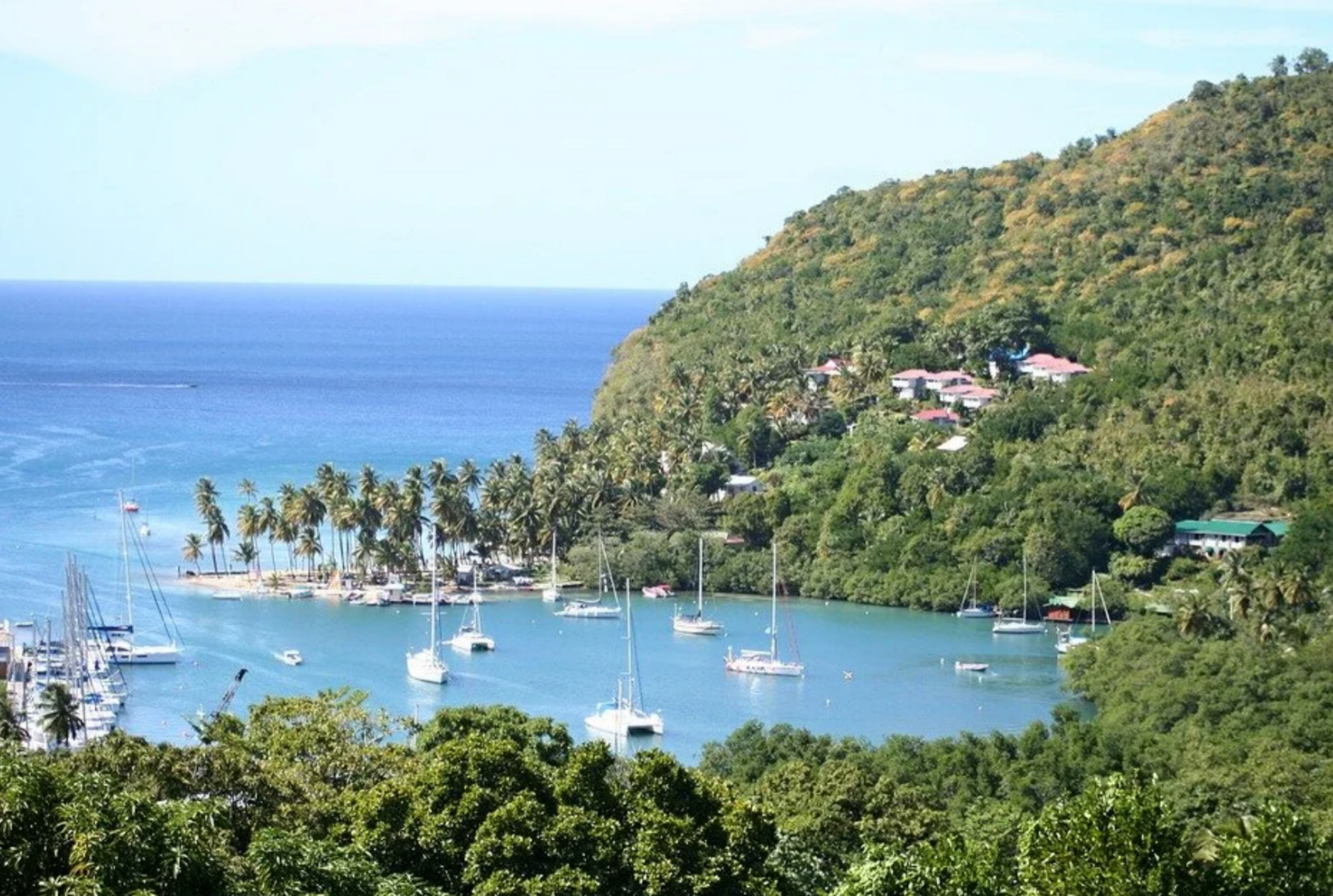 High-angle view of Marigot Bay in St. Lucia showing white sailboats anchored in a sheltered blue cove backed by steep green tropical hills.