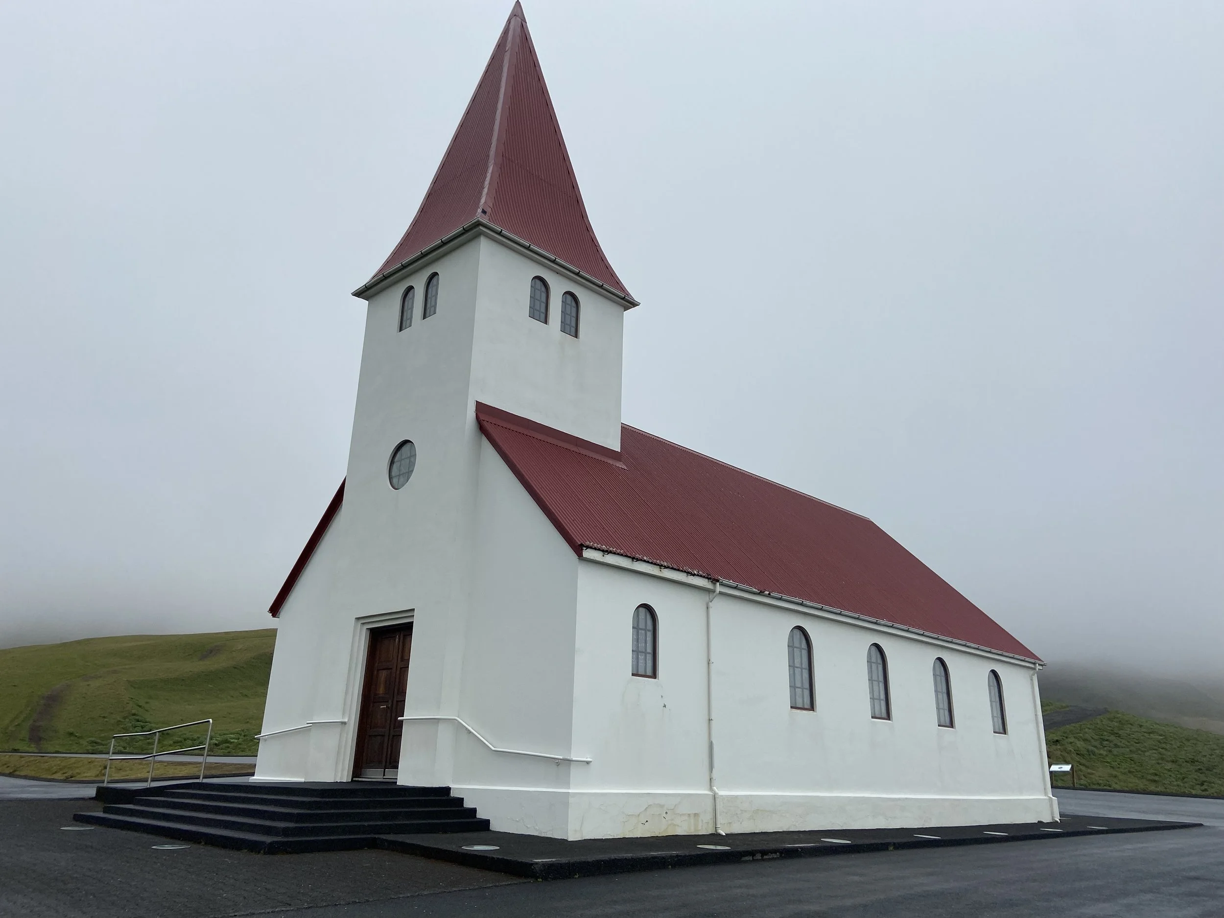 White church with a red roof and steeple under misty skies, photographed by Jeanine on her Iceland trip
