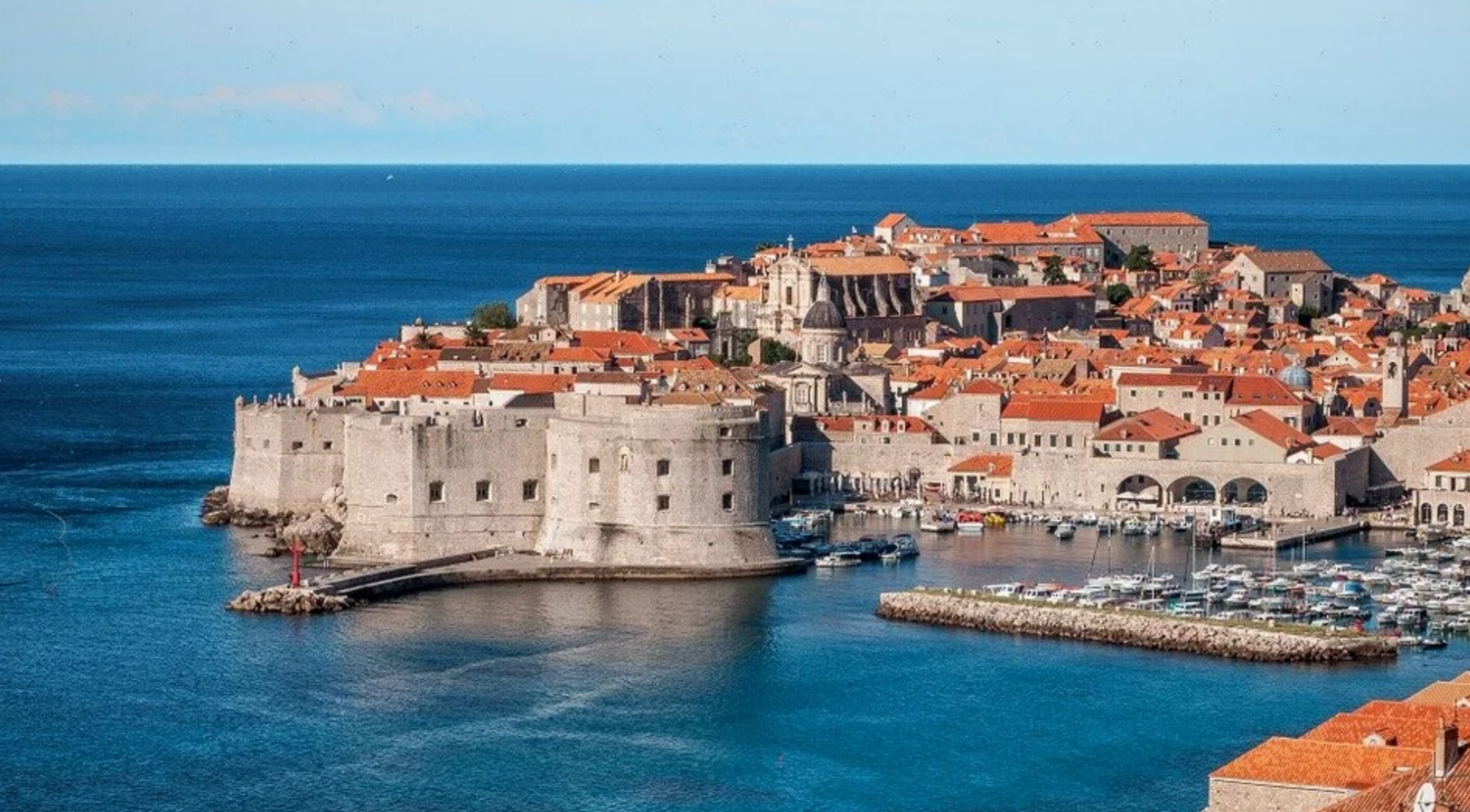 High-angle view of the historic stone wall fortress and orange terracotta rooftops of Dubrovnik Old Town surrounded by the blue Adriatic Sea in Croatia.