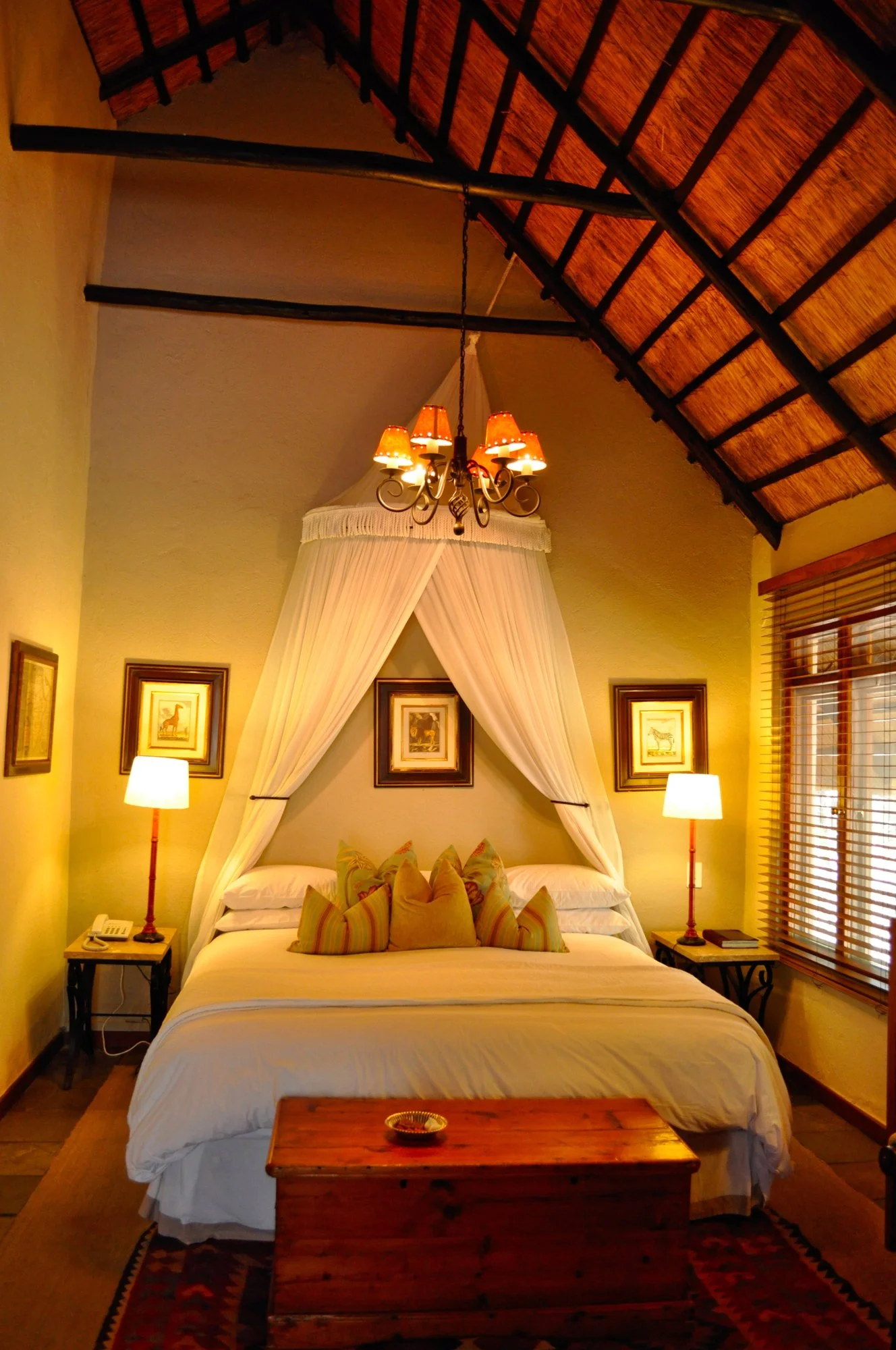 Interior of a luxury safari lodge bedroom with a canopy bed, elegant chandelier, and thatched roof, showing high-end accommodations by Lavishly Travel.