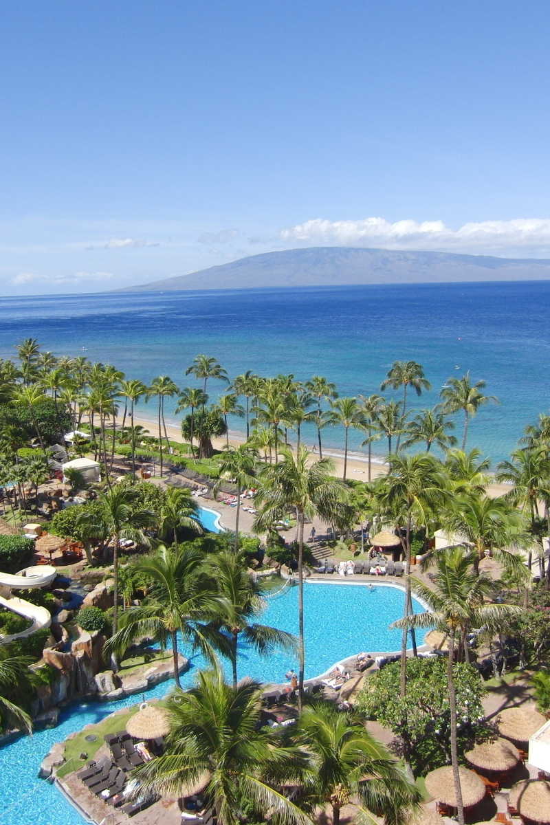 Elevated view of a luxury Hawaiian oceanfront resort in Maui featuring tropical lagoon pools, palm trees, and Ka'anapali Beach facing the island of Molokai.