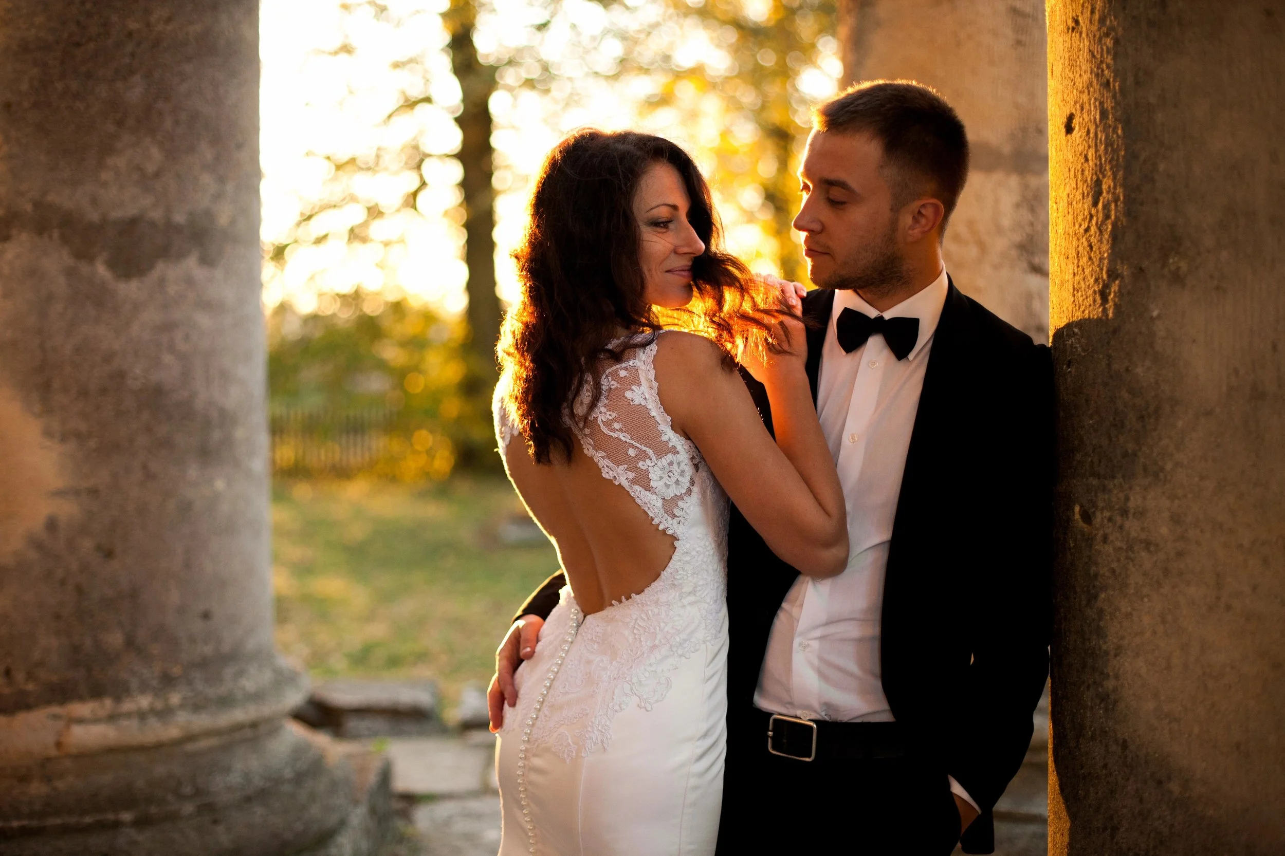 A bride in a lace gown and a groom in a tuxedo embracing during a golden hour outdoor Destination Wedding ceremony curated by Lavishly Travel