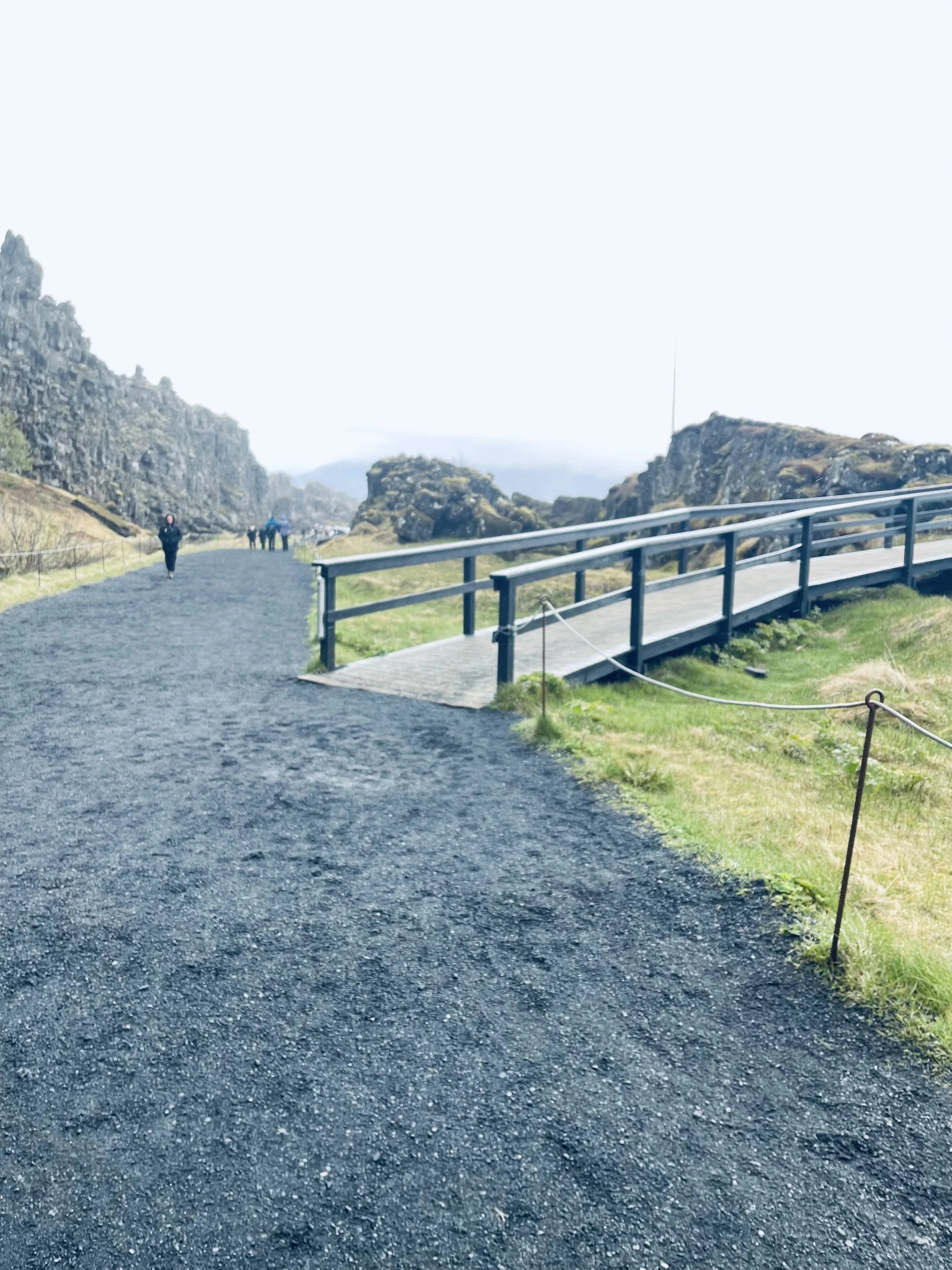 Wide walking trail and wooden railing between Icelandic rock formations, photographed by Jeanine