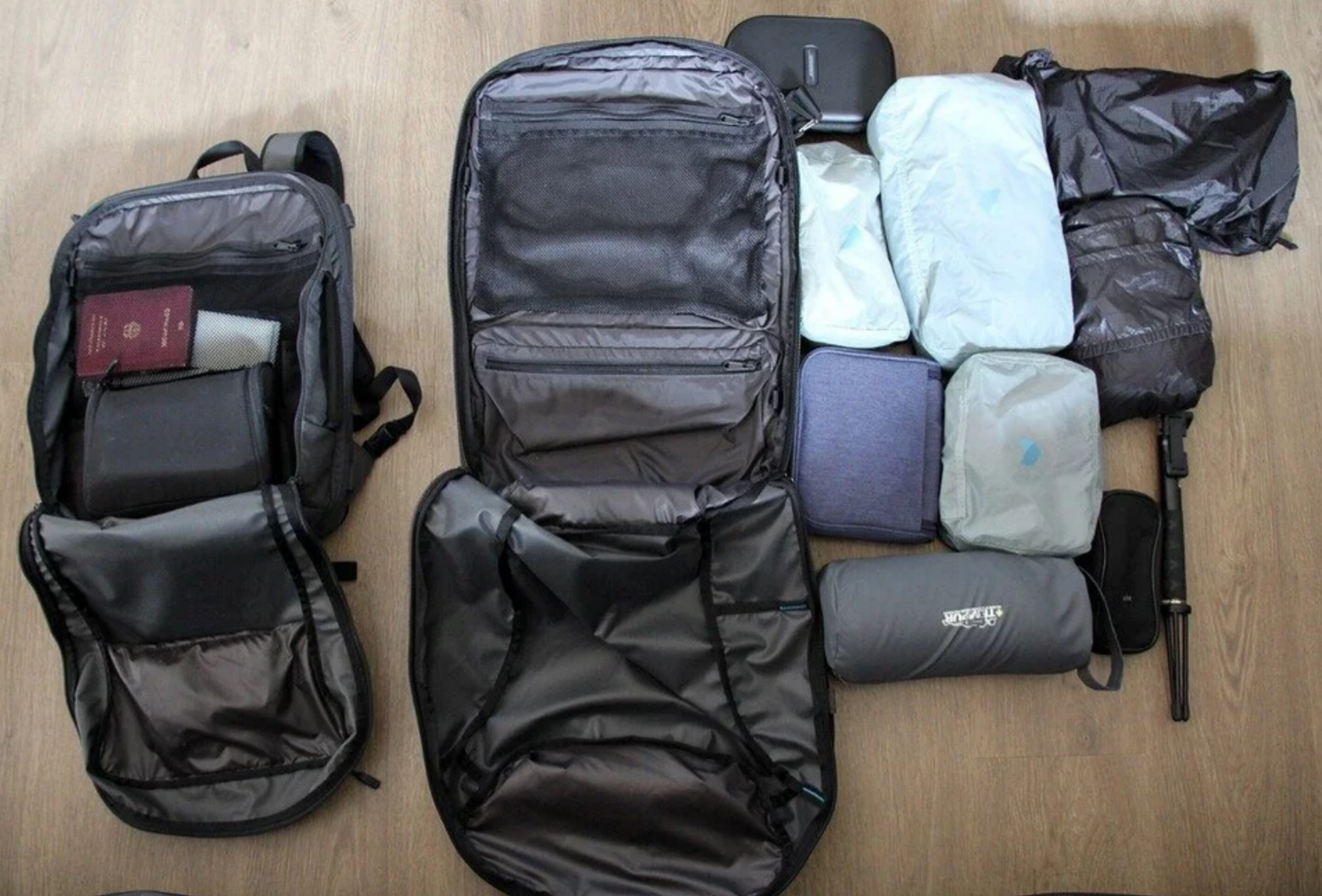 Flat lay layout of two open travel backpacks neatly organized with compression packing cubes, electronic cases, and travel gear on a wooden floor.