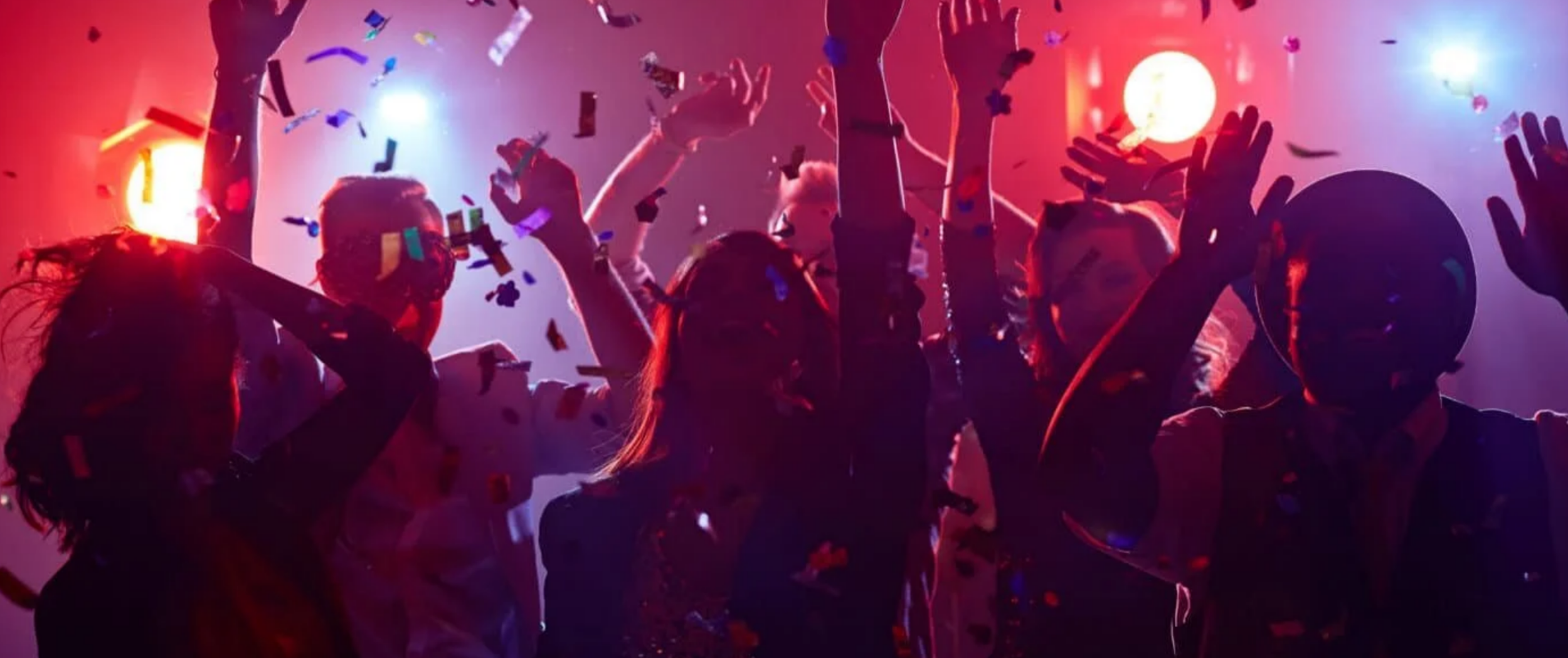 A silhouetted crowd dancing at a lively nightclub or concert venue with colorful red and blue lights and falling confetti.