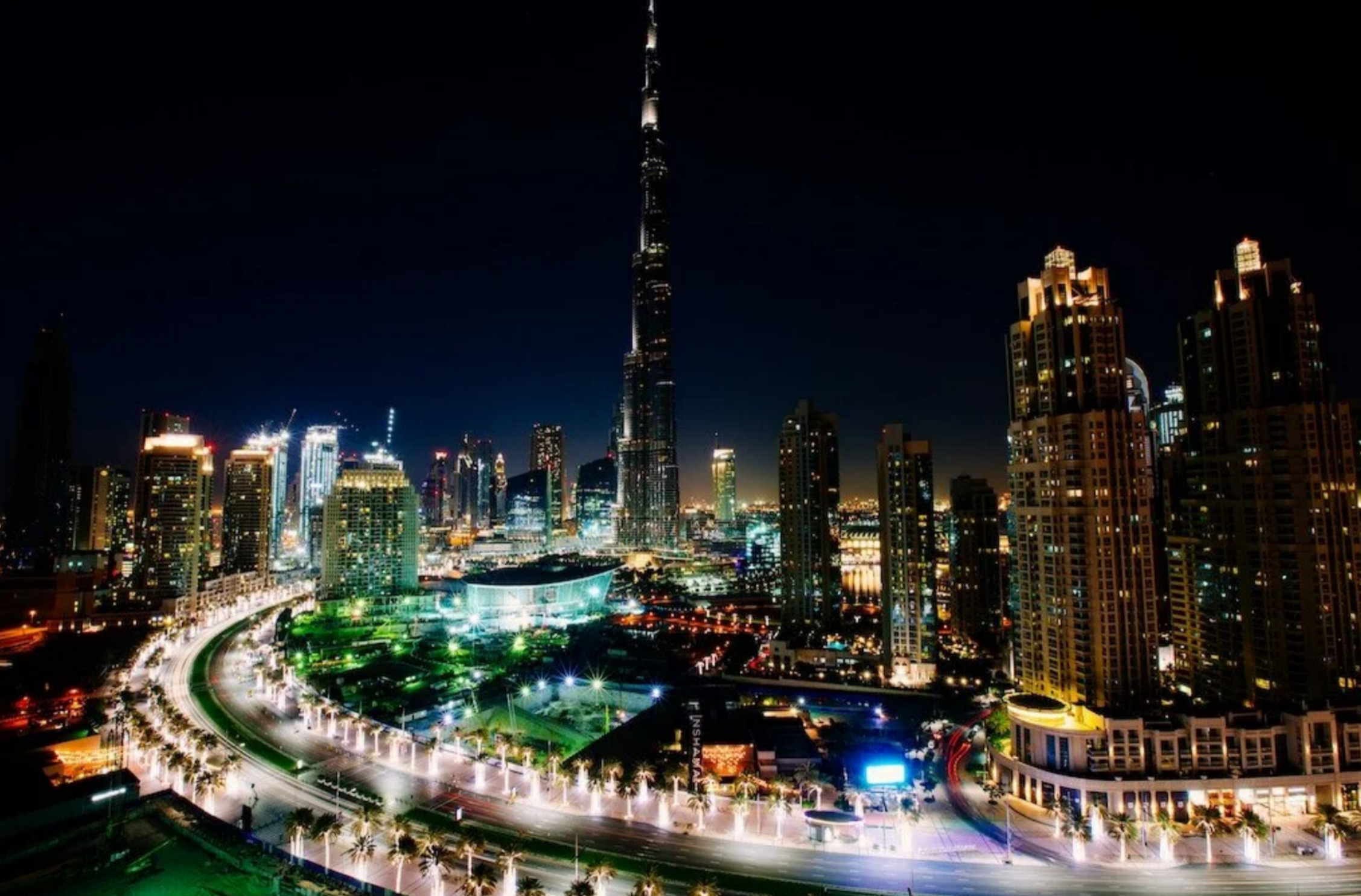 The Burj Khalifa towering over illuminated Downtown Dubai skyscrapers and a glowing curved street at night.