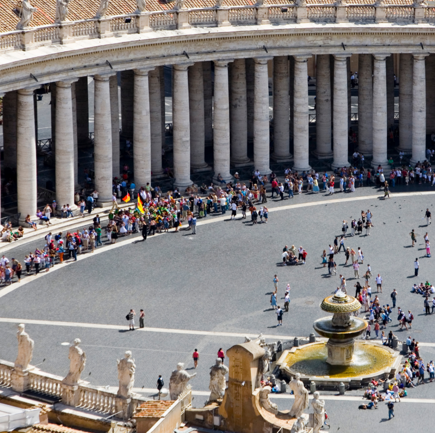 Aerial high-angle shot of tourists lining up between the grand stone colonnades and fountain in St. Peter's Square.