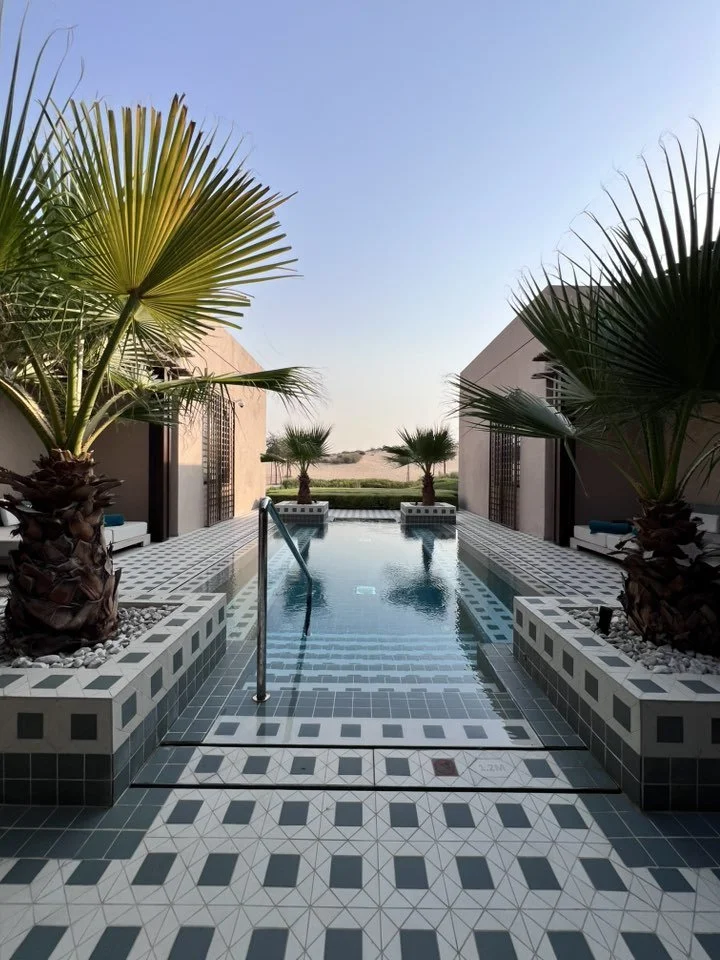 A luxury desert resort pool in Dubai with private villa architecture and palm trees.