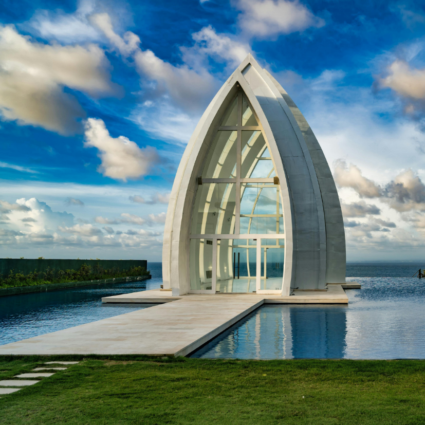 A modern, sail-shaped glass wedding chapel surrounded by an infinity pool overlooking the ocean.