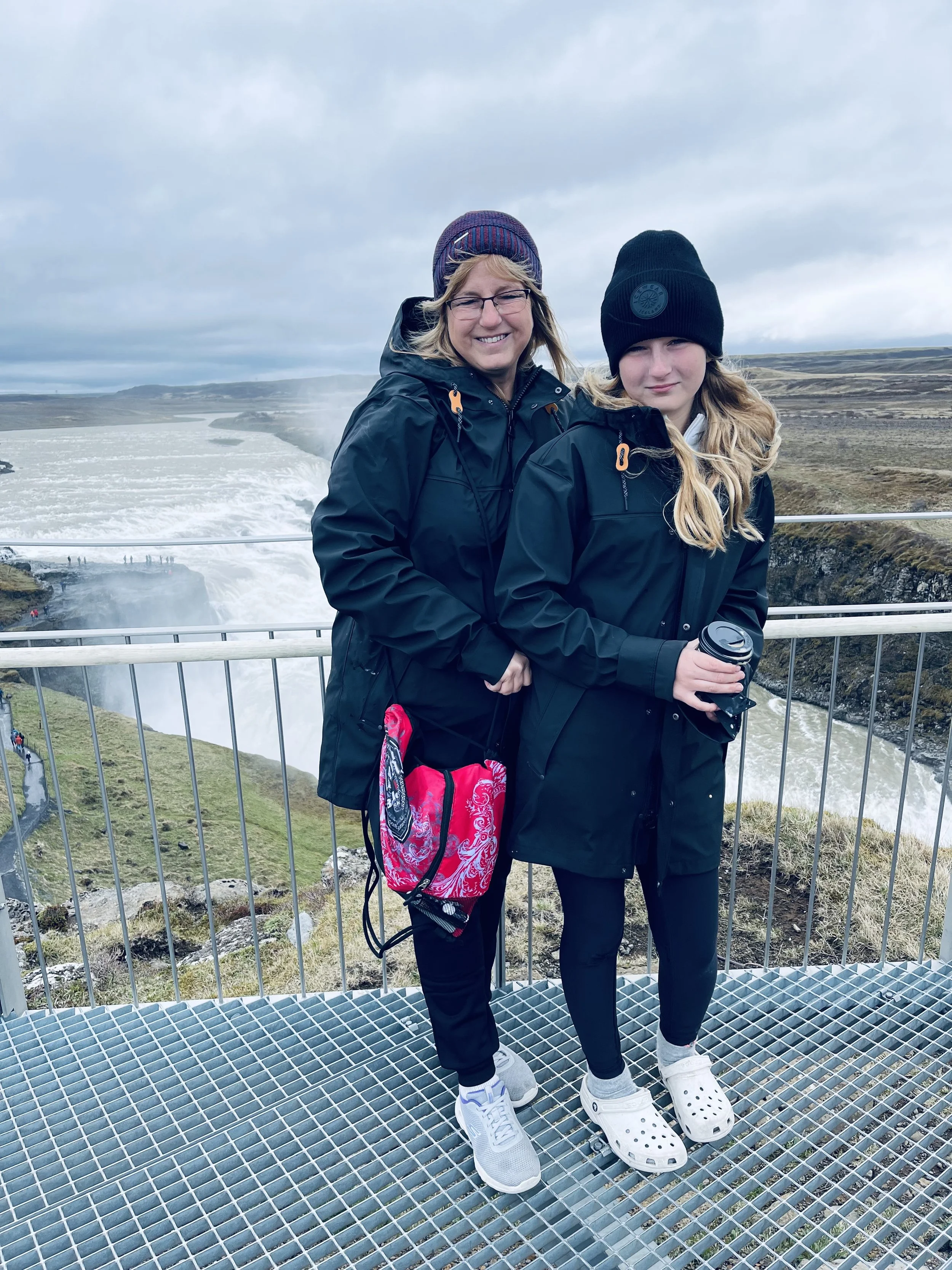 Jeanine and her daughter standing together at an Iceland waterfall viewpoint