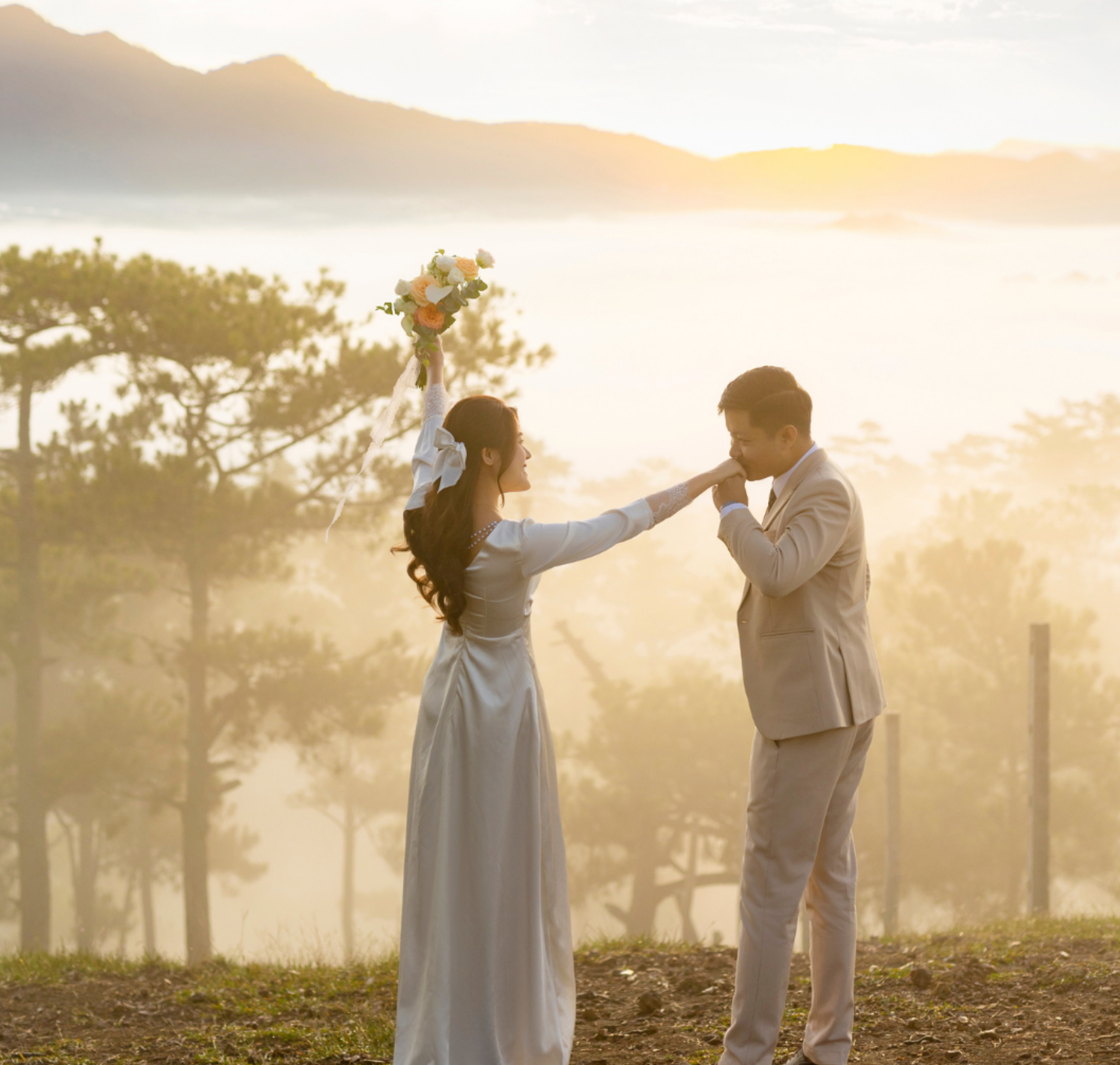 A groom kissing the bride’s hand in a misty mountain forest at sunrise during their destination wedding.