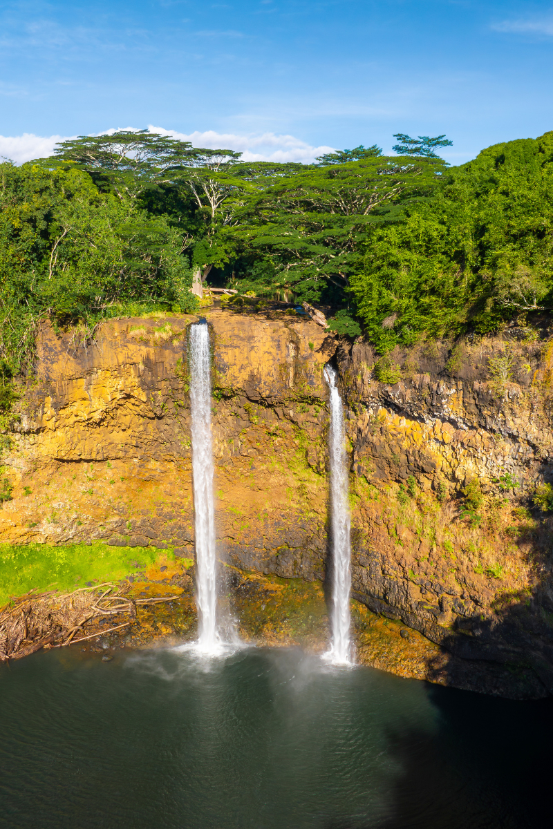 Twin streams of Wailua Falls drop over a lush volcanic cliff into a pool on Kauai, Hawaii.