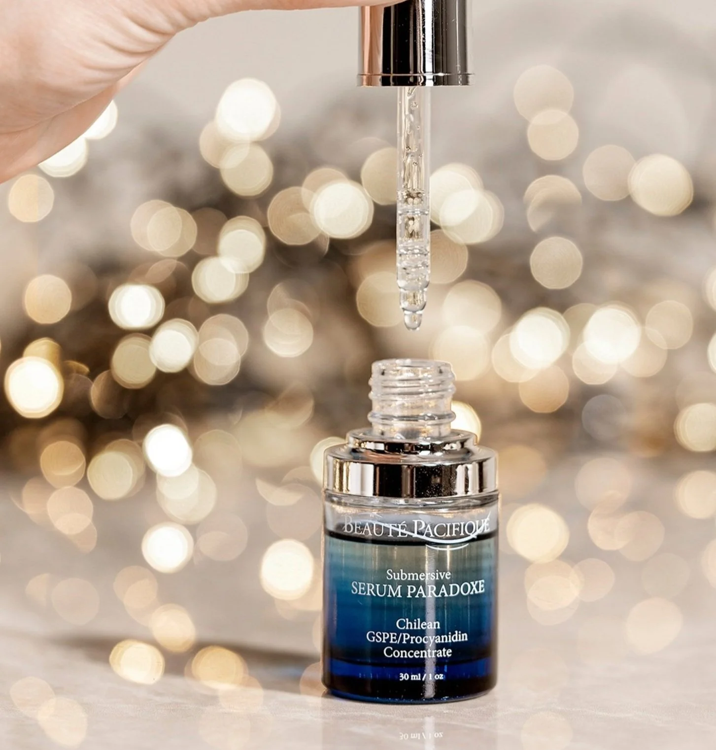 En glasflaske med serum, der har dropper ovenpå, med en bokeh baggrund af gyldne lys.