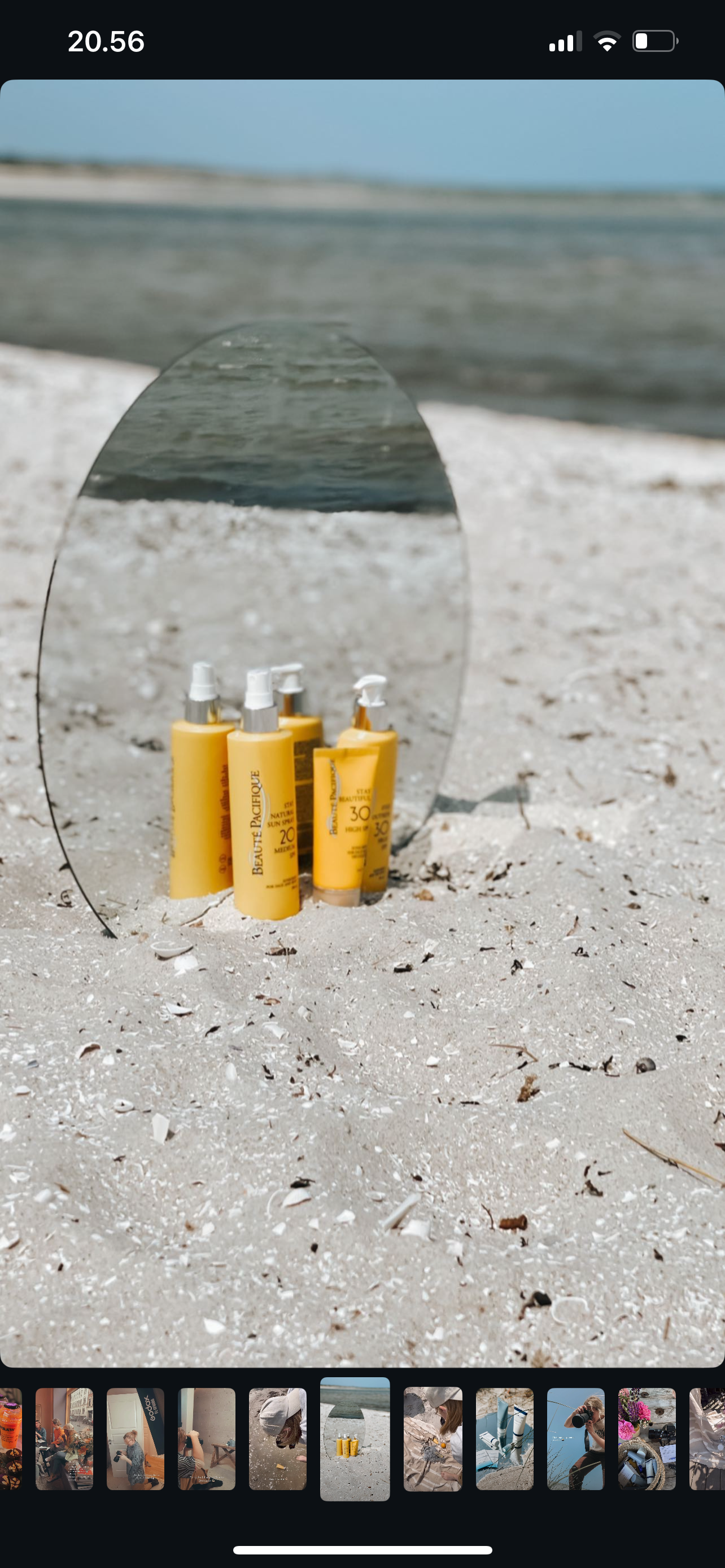 Solsikre solcremeflasker på sand med havudsigt i baggrunden, spejlet reflekterer flaskerne.