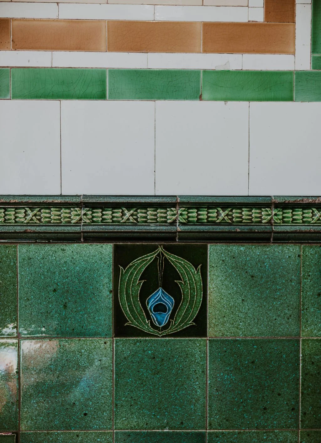 Close-up of decorative green and white tiled wall with a central decorative tile featuring a peacock feather design.