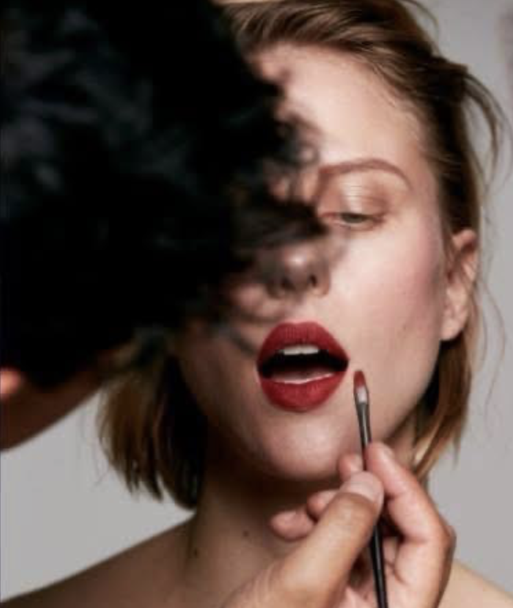 A woman getting her makeup done, with a makeup artist applying lipstick with a small brush.