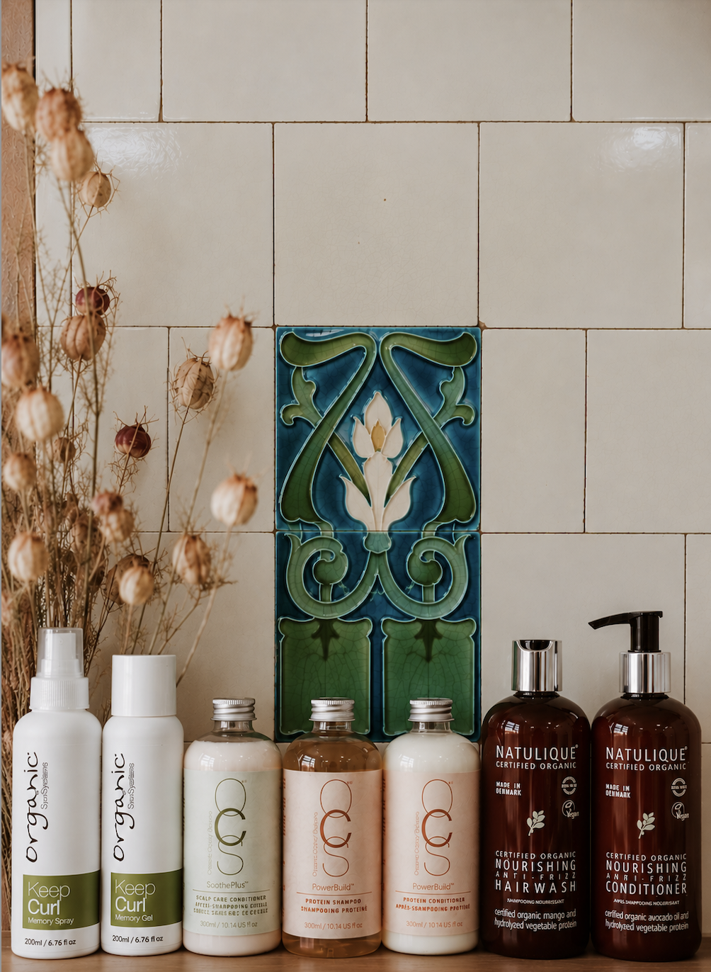Row of hair and skincare products on a shelf against a tiled wall with decorative tiles.