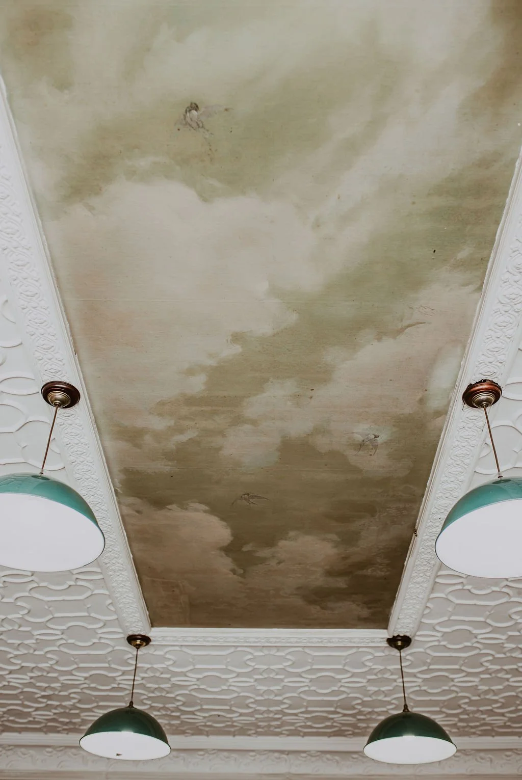 Ceiling with water damage and stains, surrounded by decorative crown molding and hanging light fixtures.