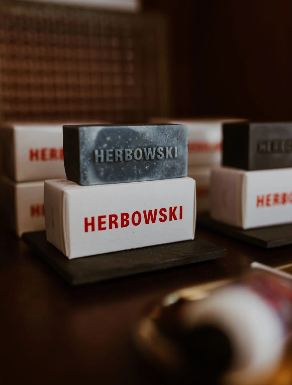 Stacks of soap bars labeled 'Herbowski' on a black display, with a dark background and blurred objects in the foreground.