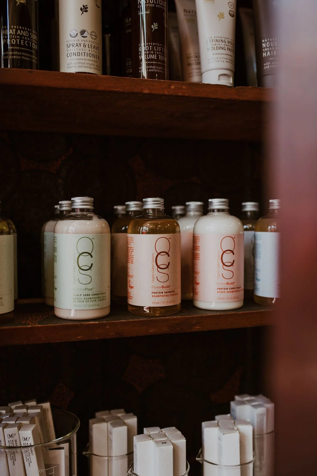 Shelf with bottles of hair care products, including shampoo and conditioner, in a store or salon.