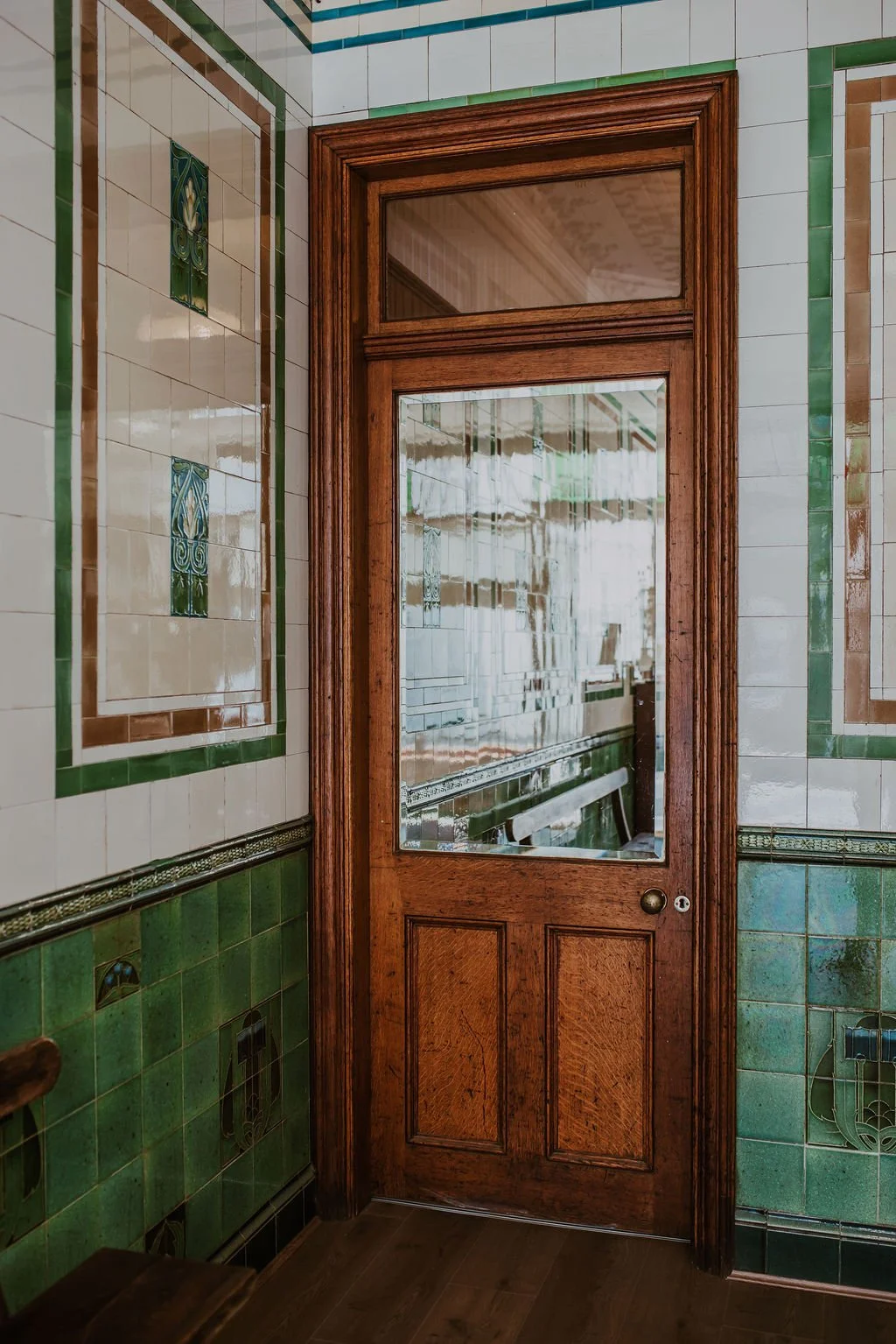 Wooden door with glass pane in an ornately decorated tiled wall.