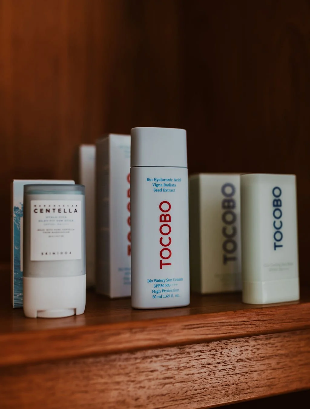 Skincare products placed on a wooden shelf, including bottles and boxes of TocoBO, Centella, and other skincare brands.