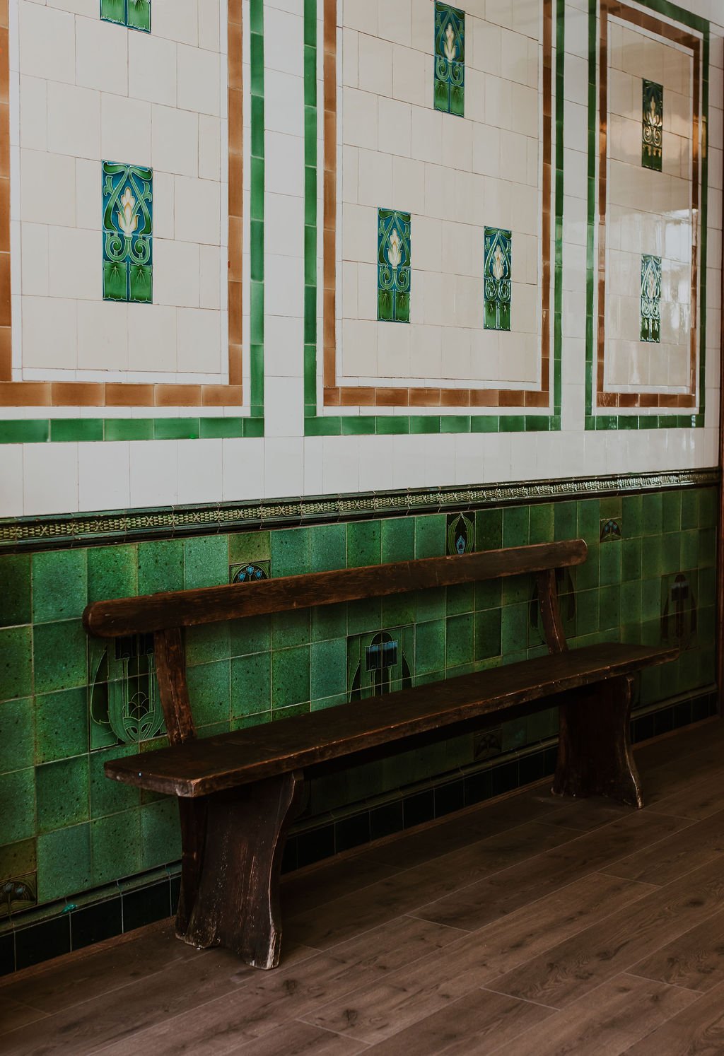 Wooden bench in front of a decorative green and white tiled wall with patterned accents.