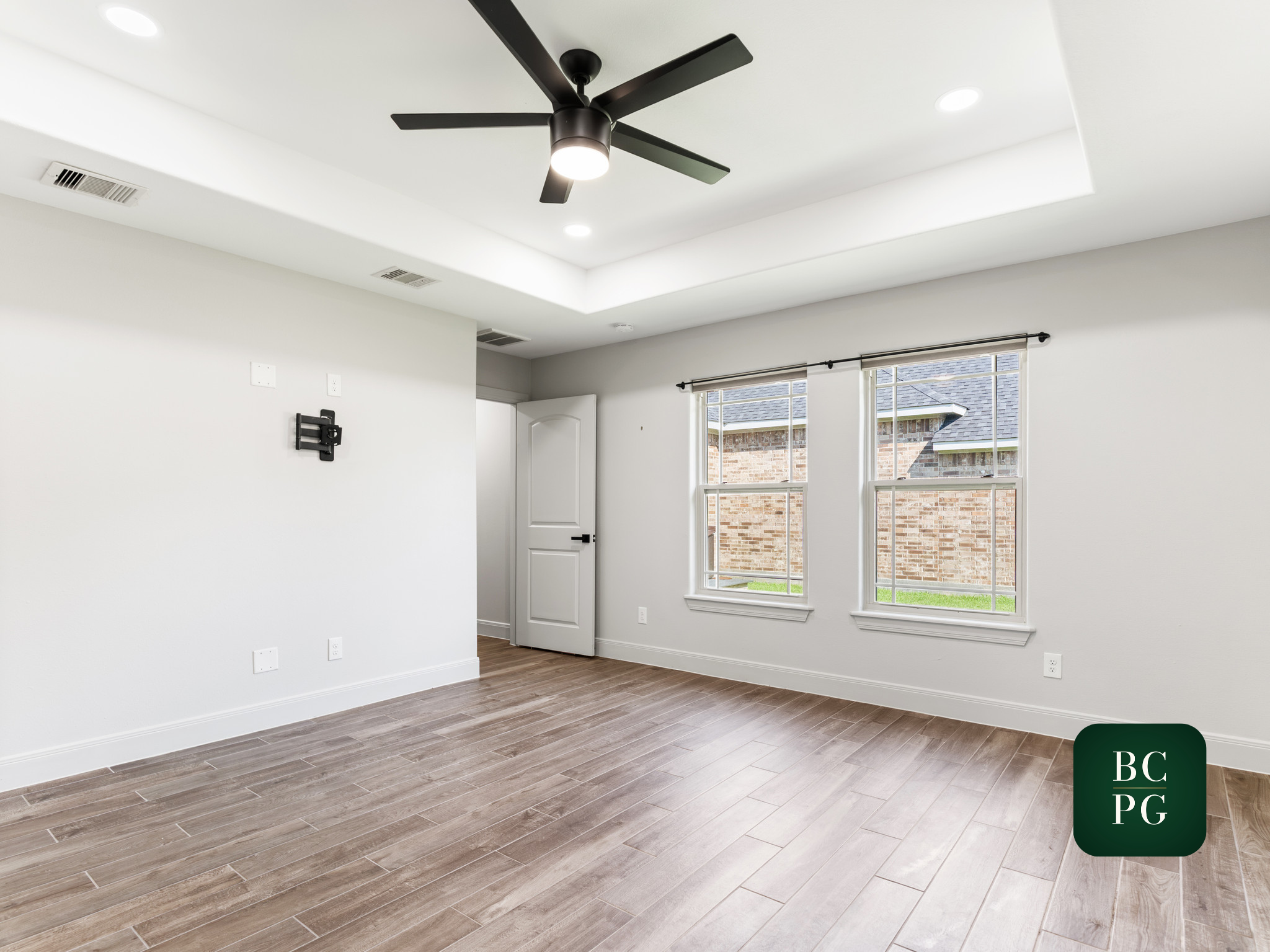 Empty room with large windows, white walls, ceiling fan, and wood flooring.